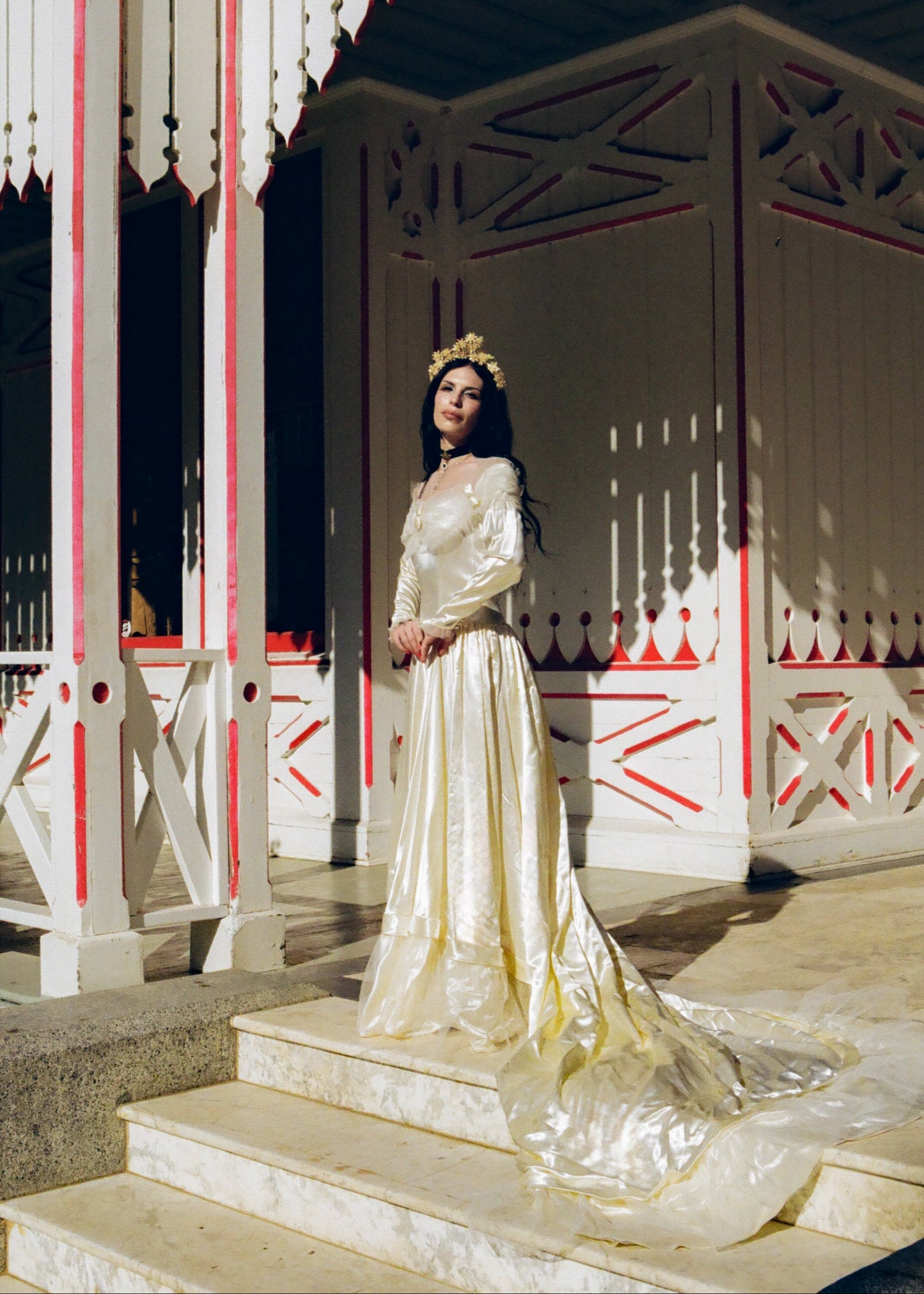 Woman in a white gown standing on steps with a decorative background