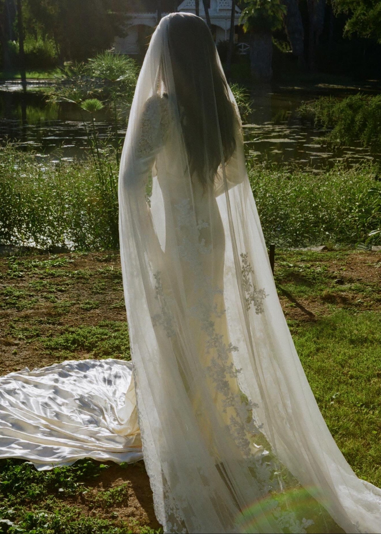 Person wearing a long, white wedding dress with a lace veil in a natural setting.