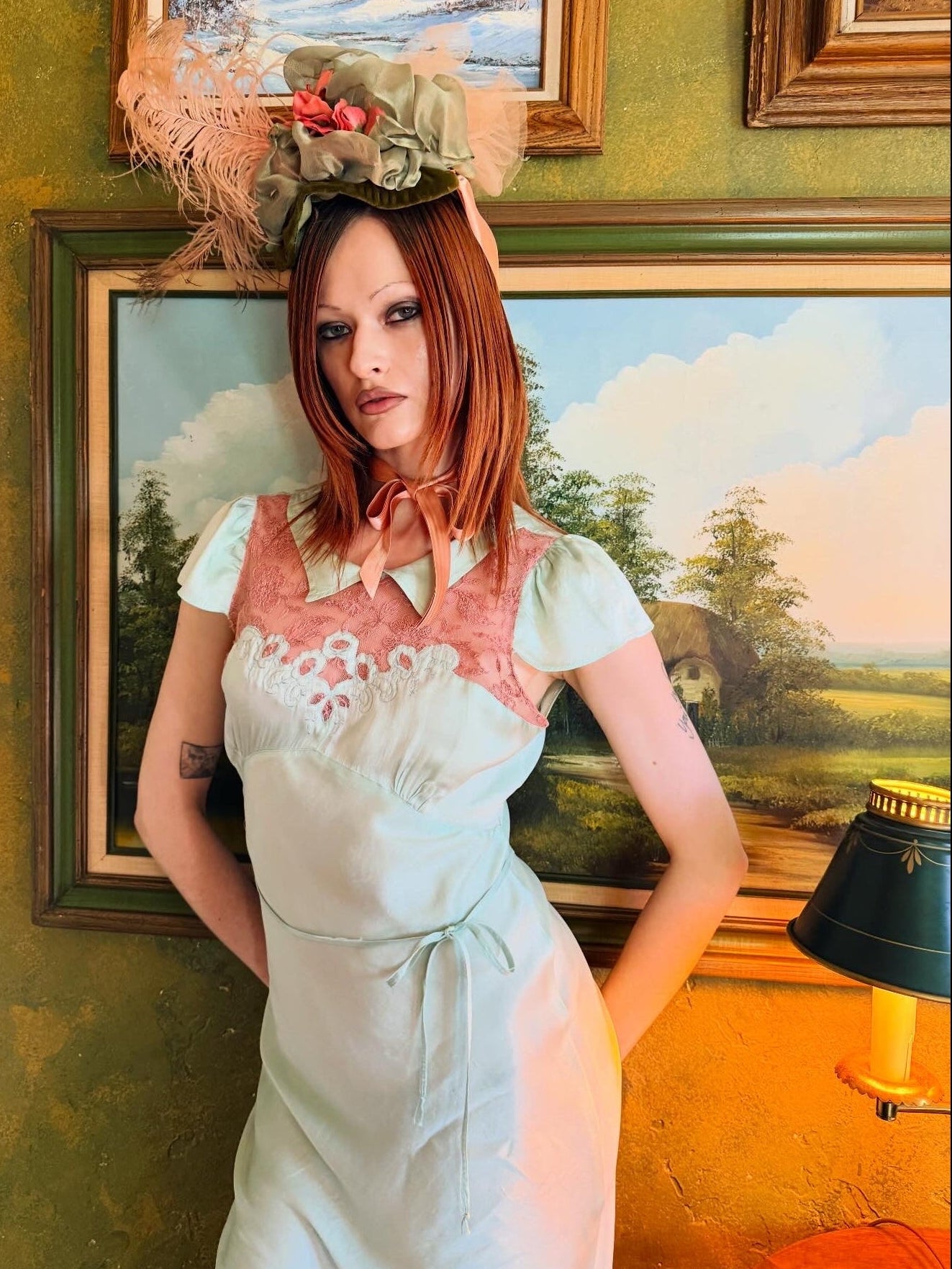 Woman in an antique 1930's silk slip in mint green with a floral headpiece against a wall with framed paintings.