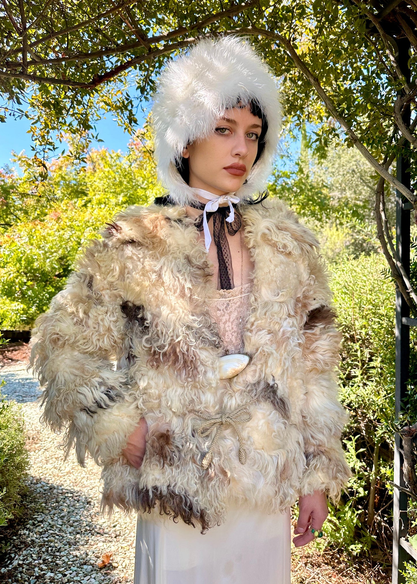Person wearing a fur coat and white hat outdoors with trees in the background
