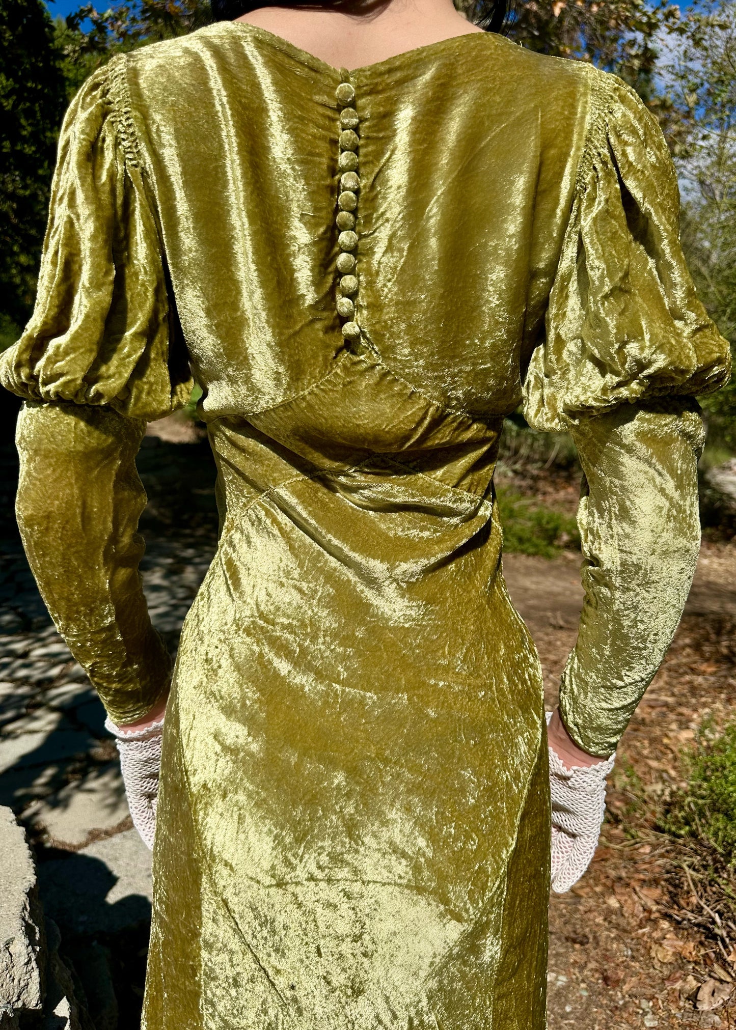 Green antique 1930s velvet dress with long sleeves and button details, worn outdoors.