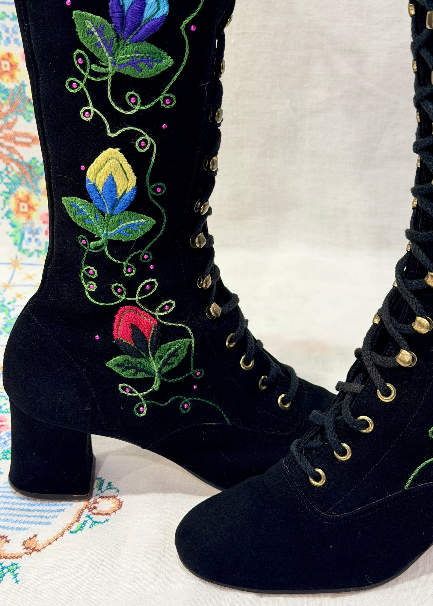 Black knee-high 1960's suede penny lane gogo boots with colorful floral embroidery on a decorative background