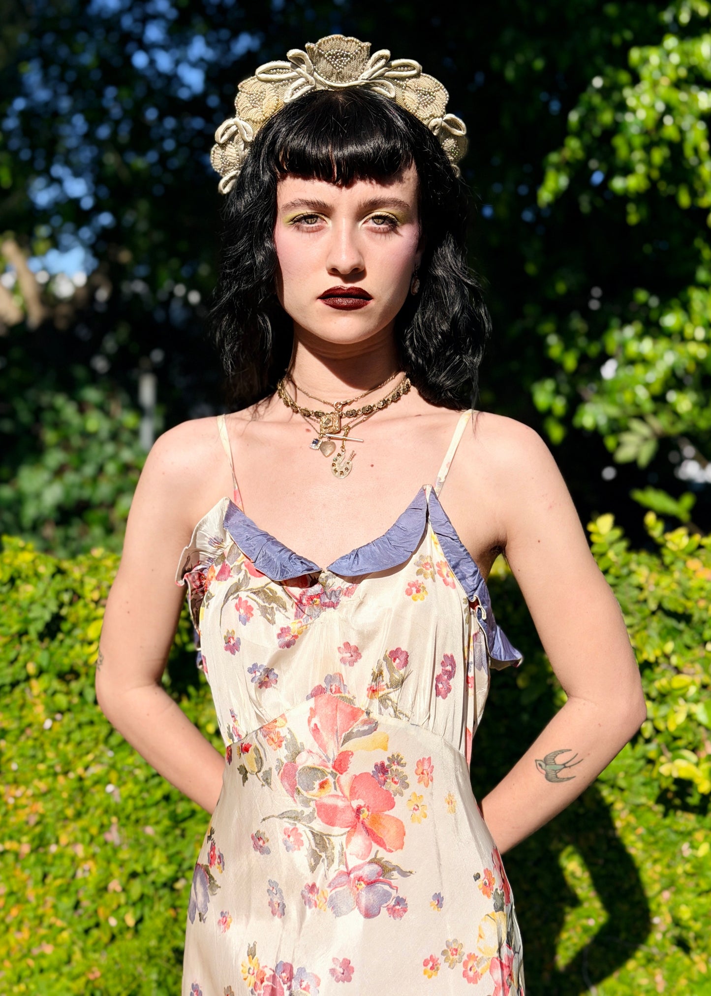 Woman wearing a floral dress and decorative headpiece outdoors with greenery in the background