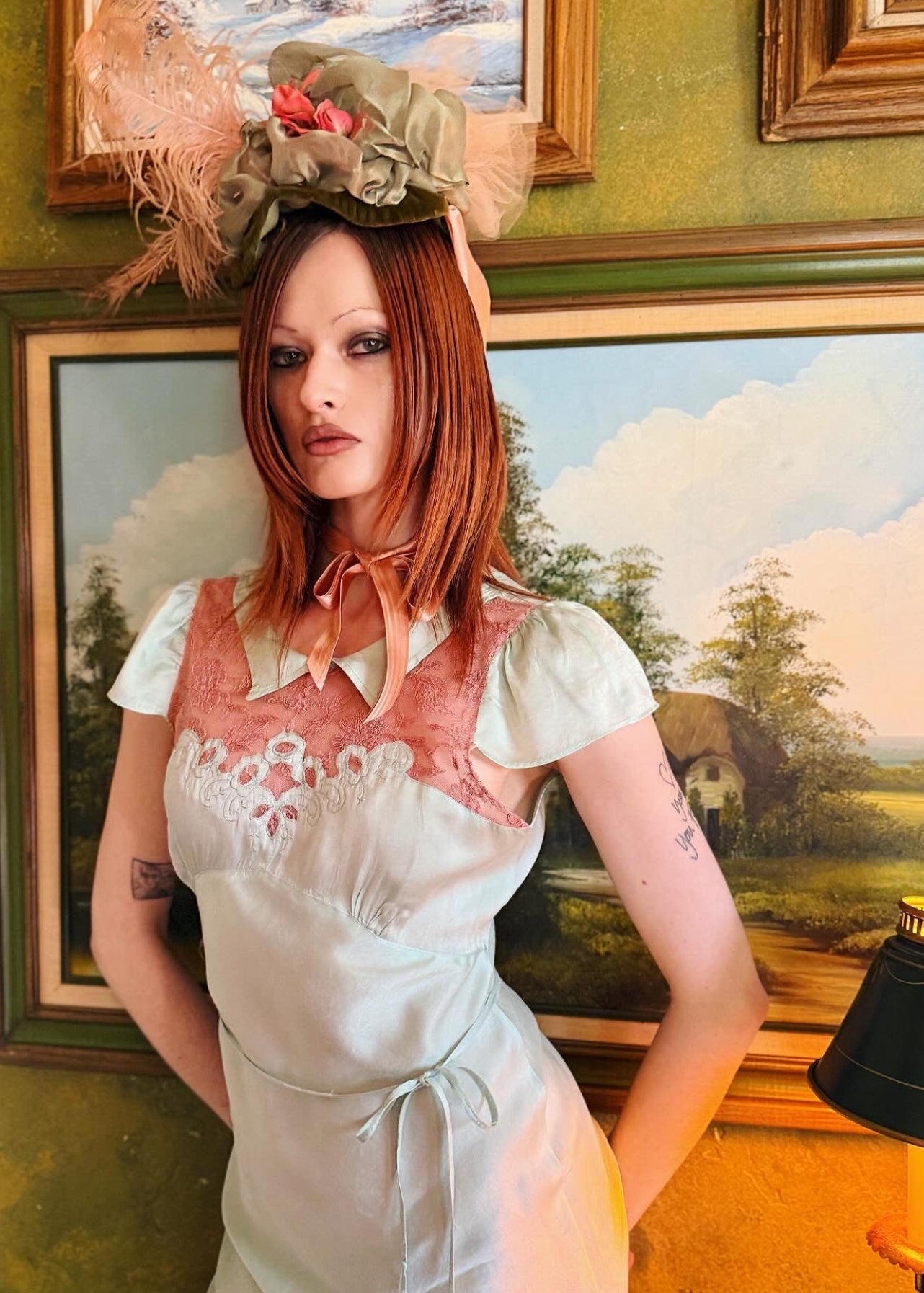 Woman in an antique 1930's silk slip in mint green with a floral headpiece against a wall with framed paintings.