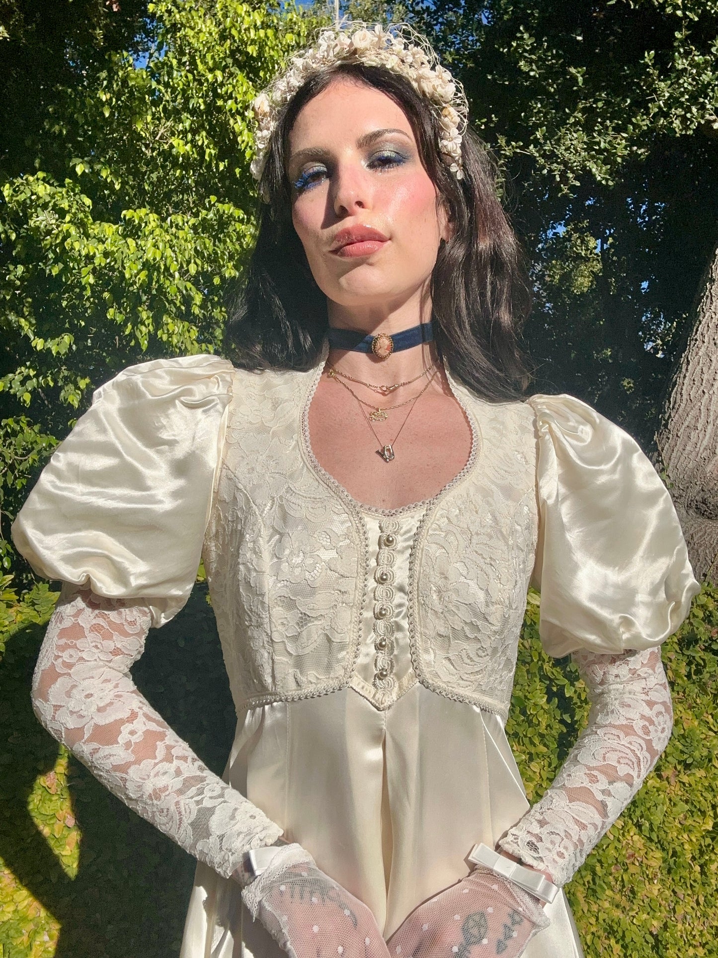 Woman in a vintage-style dress with lace sleeves and gloves standing outdoors.