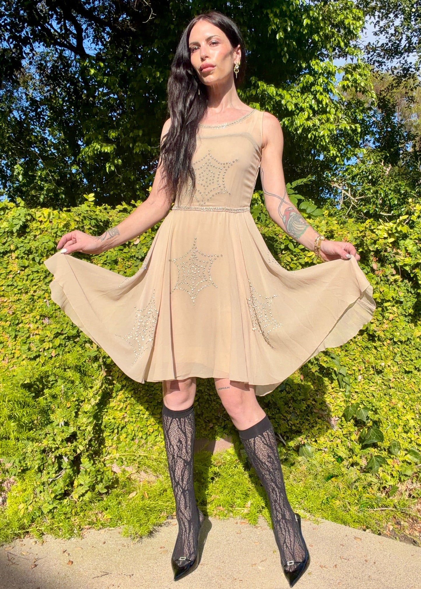 Beige antique 1920's silk chiffon dress with star or spider web design embellishments made from rhinestones worn by a person outdoors.