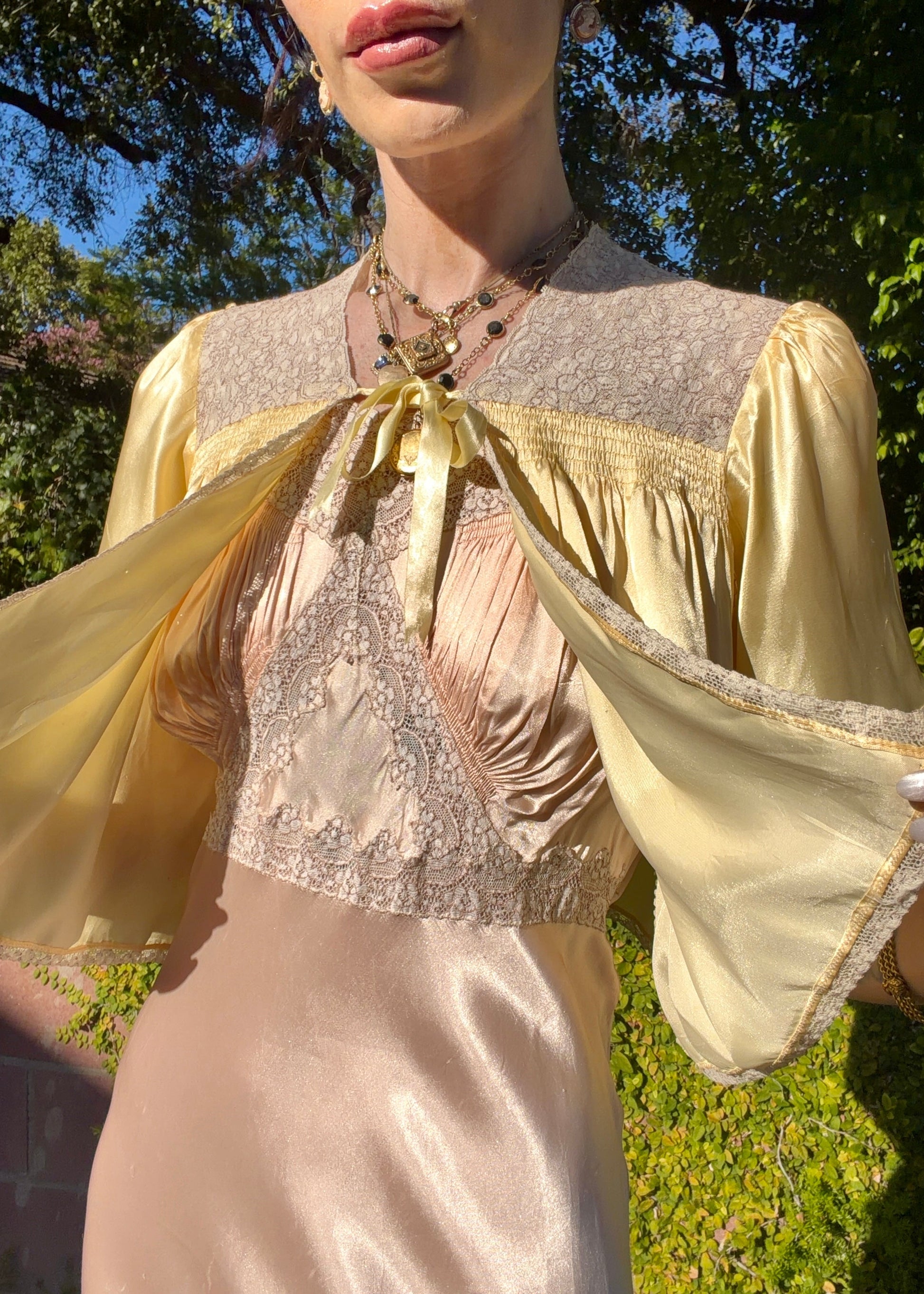 Woman wearing a long bias cut, elegant antique 1930's silk slip dress in a light pink color in an outdoor setting.
