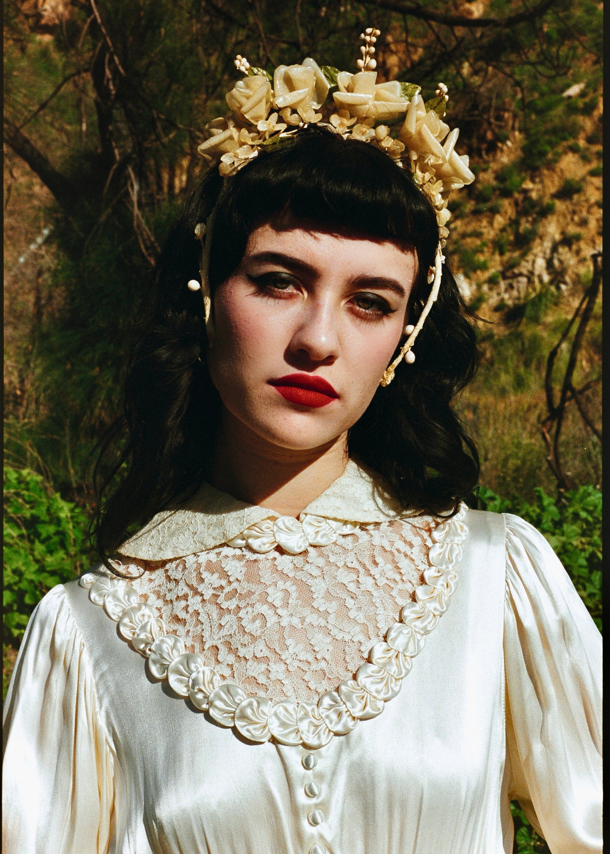 Woman wearing a white lace dress and headpiece with flowers outdoors