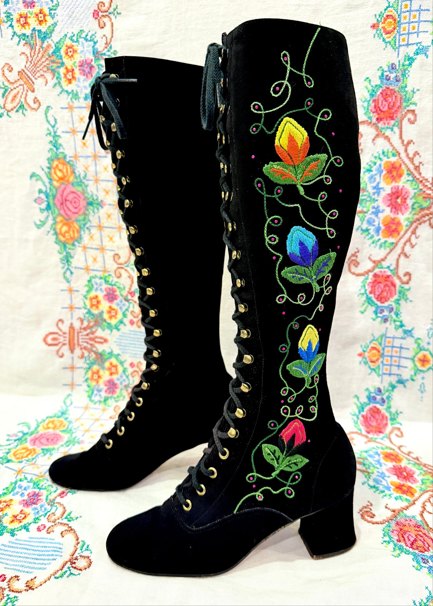 Black knee-high vintage 1960's suede penny lane gogo boots with colorful floral embroidery on a decorative background