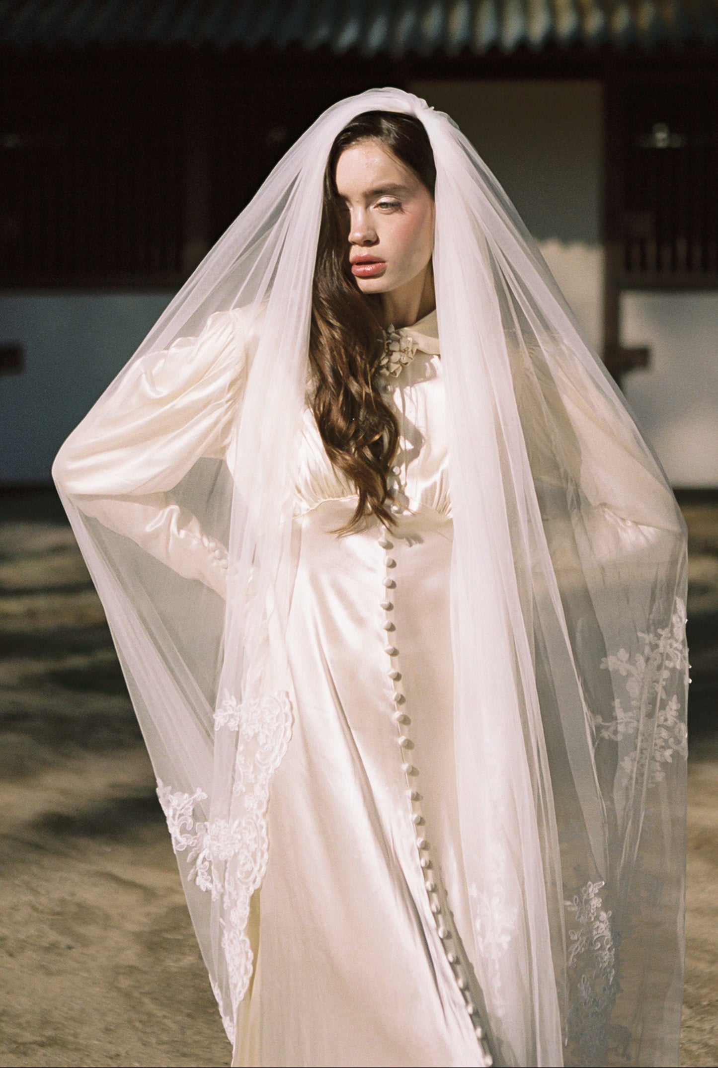 Woman wearing a white lace dress with a veil in front of a traditional building.