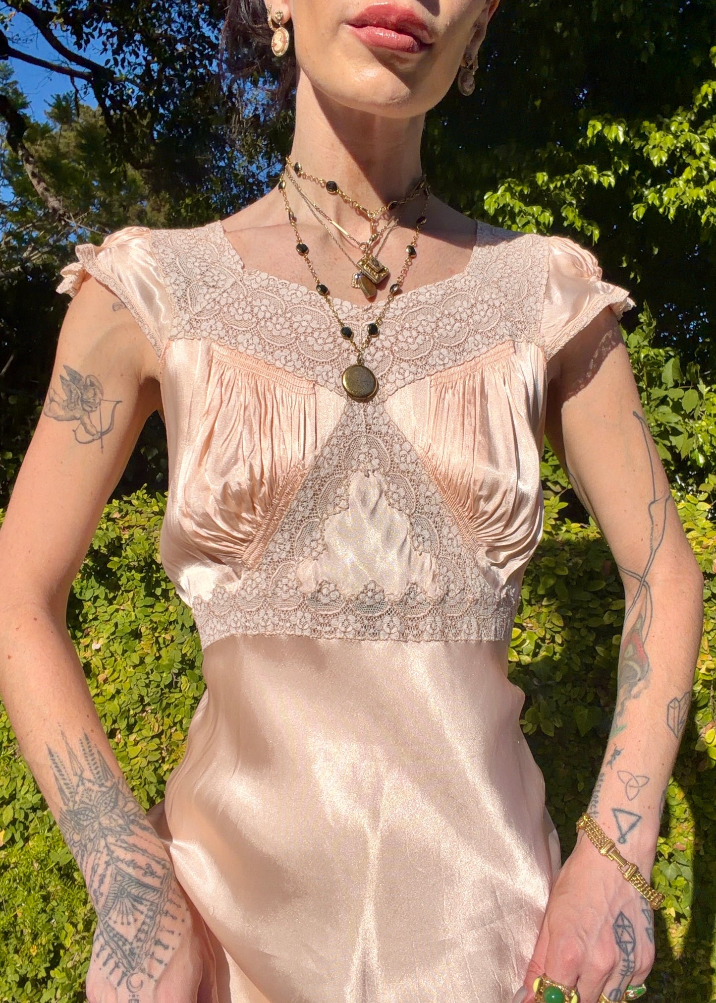 Woman wearing a long bias cut, elegant antique 1930's silk slip dress in a light pink color in an outdoor setting.