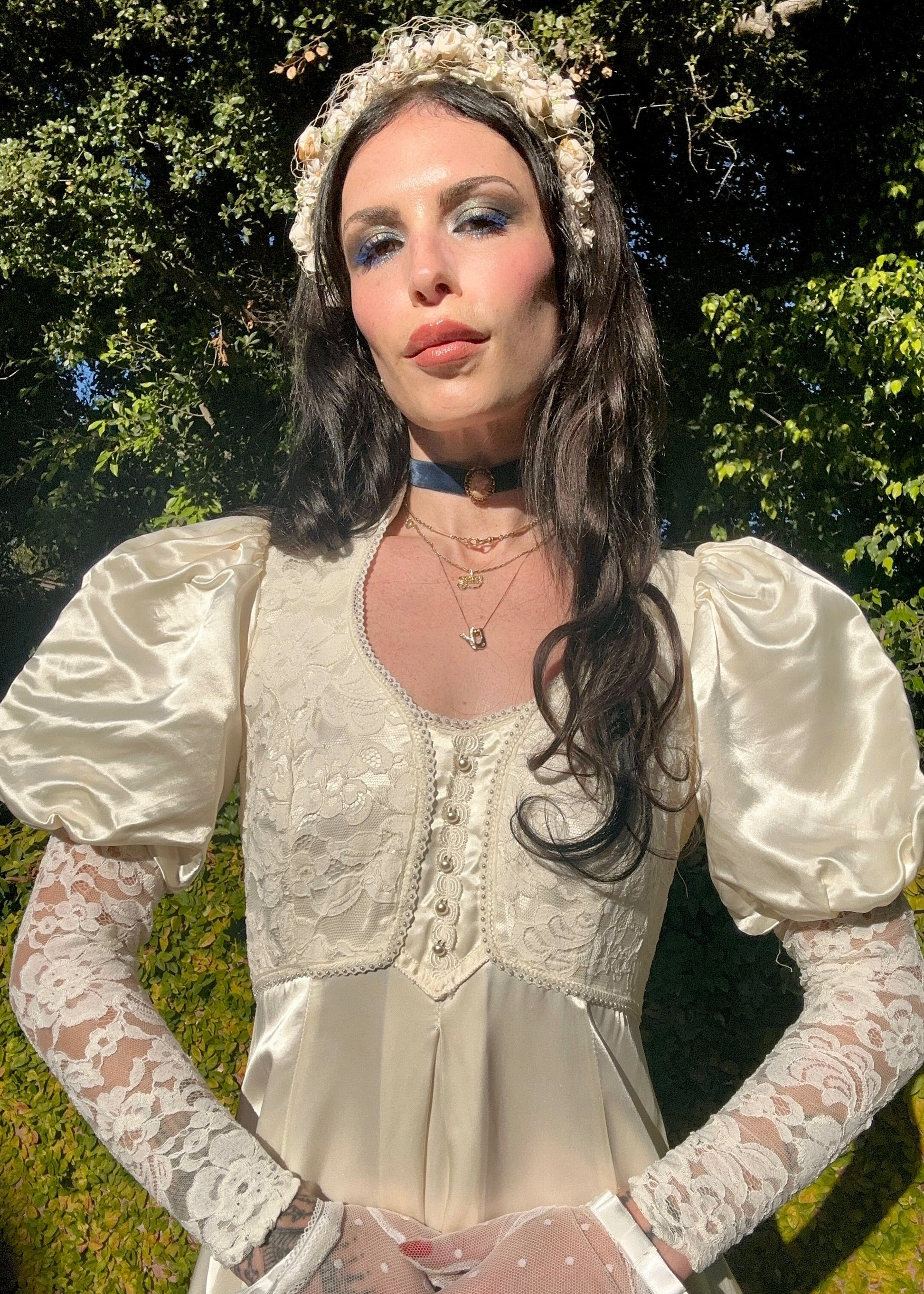 Woman in a vintage-style dress with lace sleeves and a headpiece outdoors.