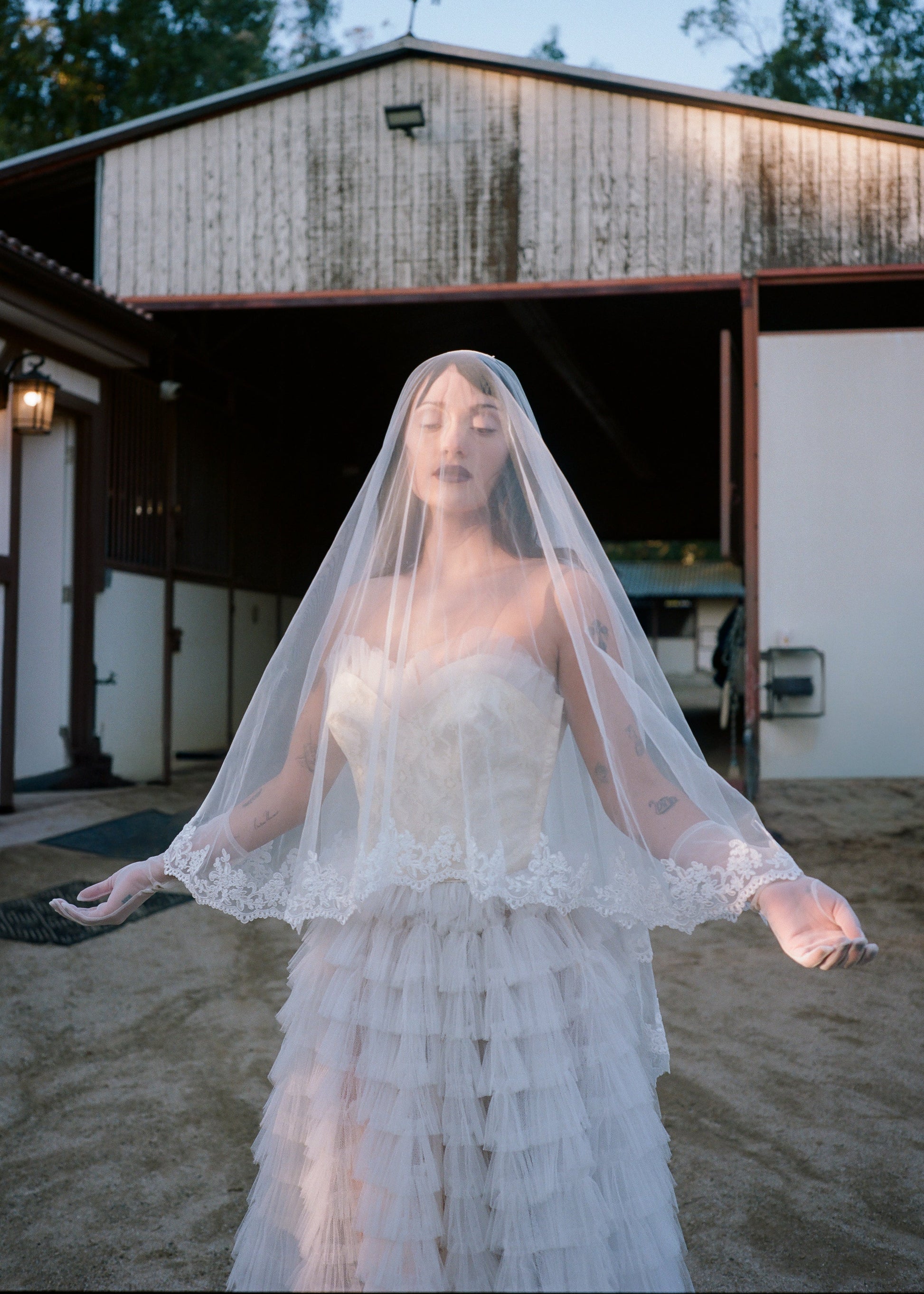 Woman in a vintage wedding dress with a veil standing in front of a rustic building.