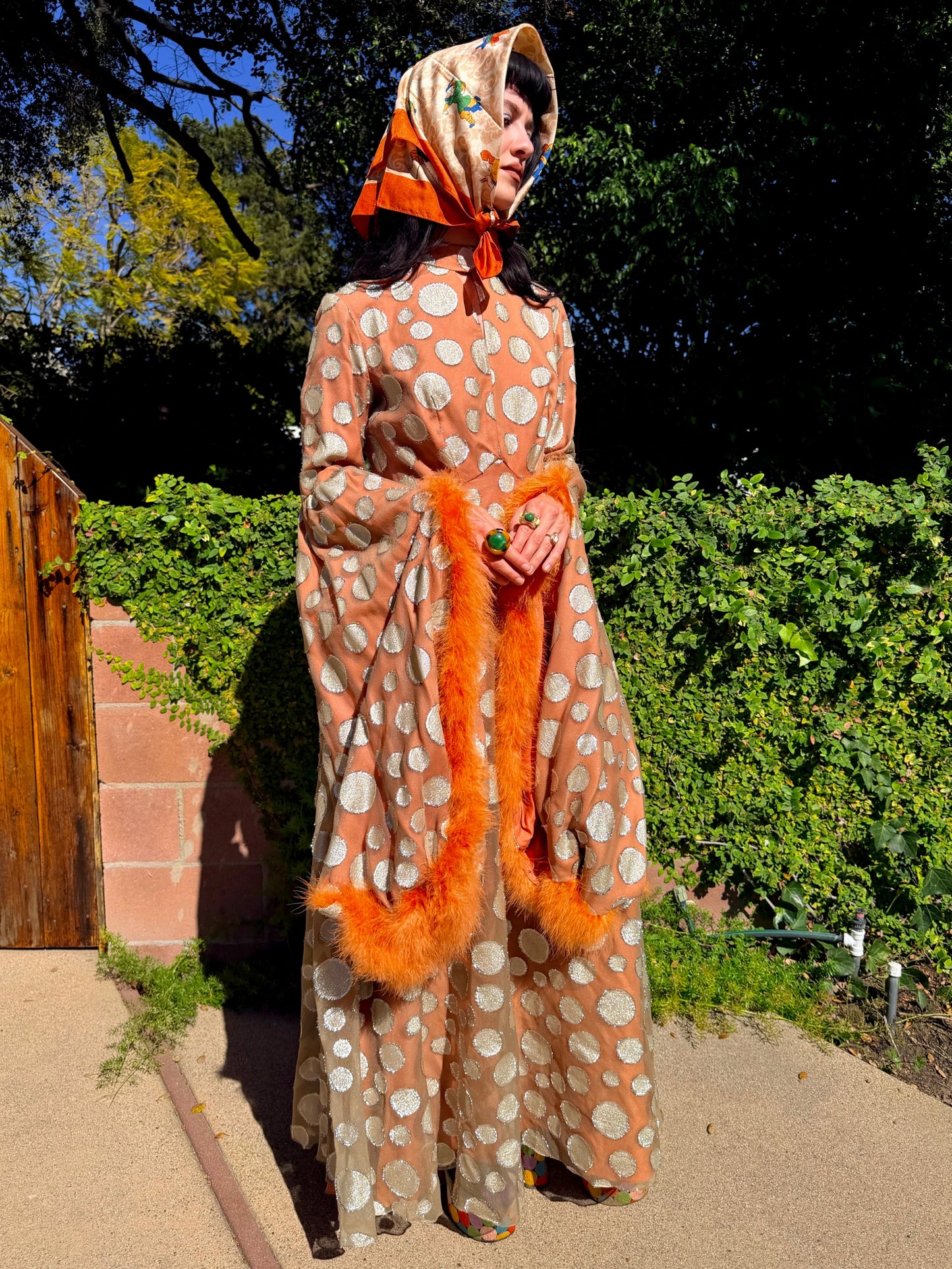 Woman in a vintage 1970s disco glamorous maxi dress with polka dots and orange accents standing outdoors.