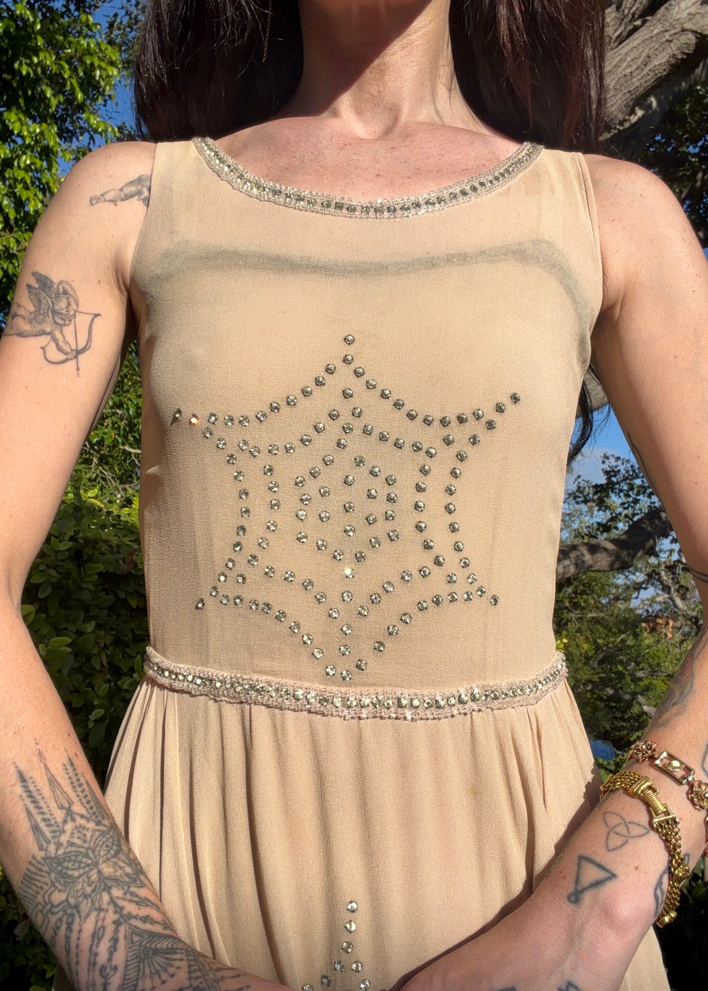 Beige antique 1920's silk chiffon dress with star or spider web design embellishments made from rhinestones worn by a person outdoors.
