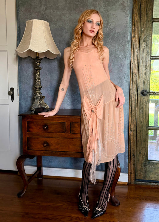 Woman in a beige dress standing in a room with wooden floor and gray walls.