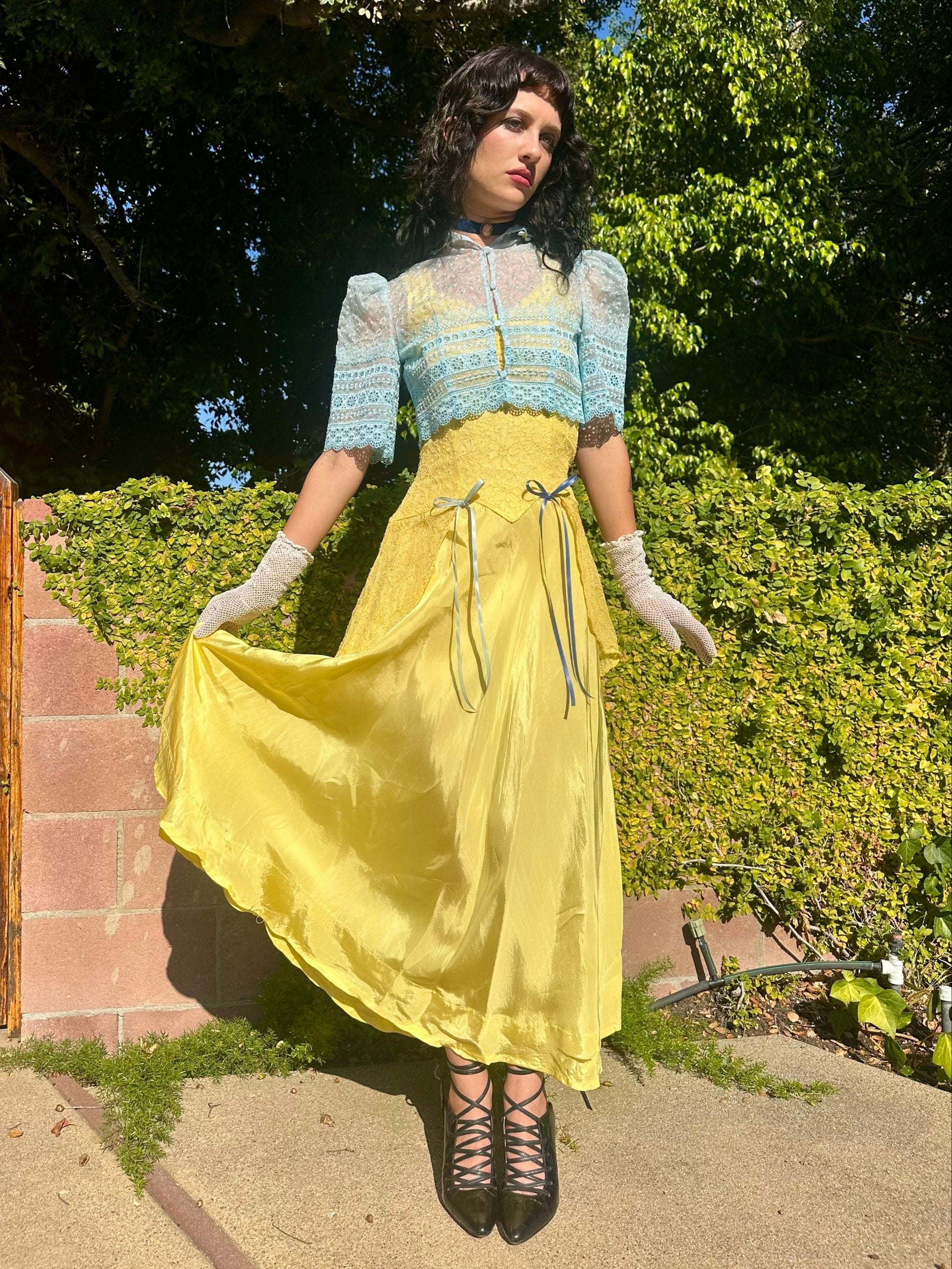 Woman in a vintage-style dress standing outdoors with greenery in the background