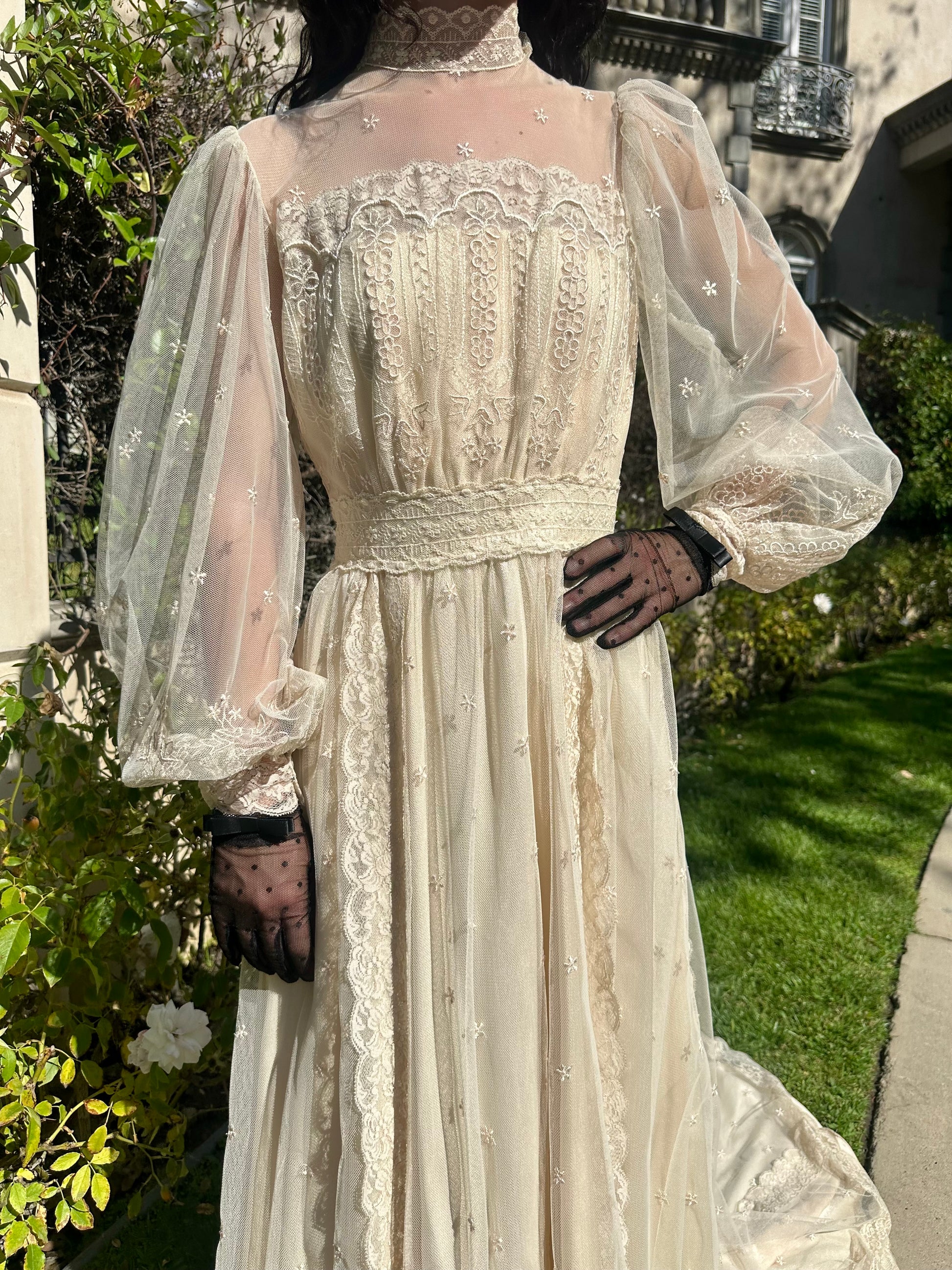 Vintage-style dress with sheer sleeves and intricate detailing in an outdoor setting.