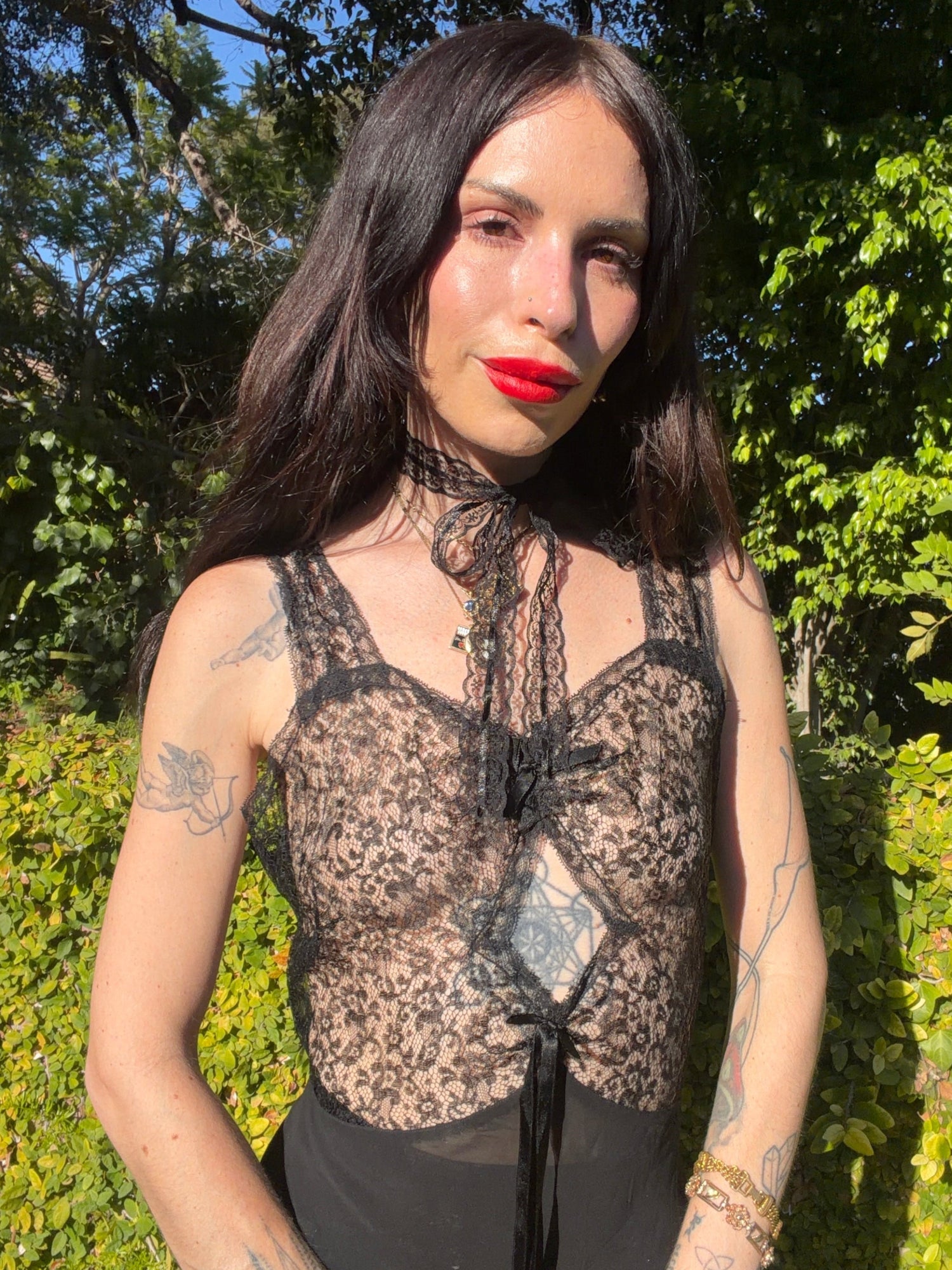 A woman with long dark hair and tattoos wearing an antique 1930's sheer black lace corset top with a tie-neck detail, and silk chiffon skirt