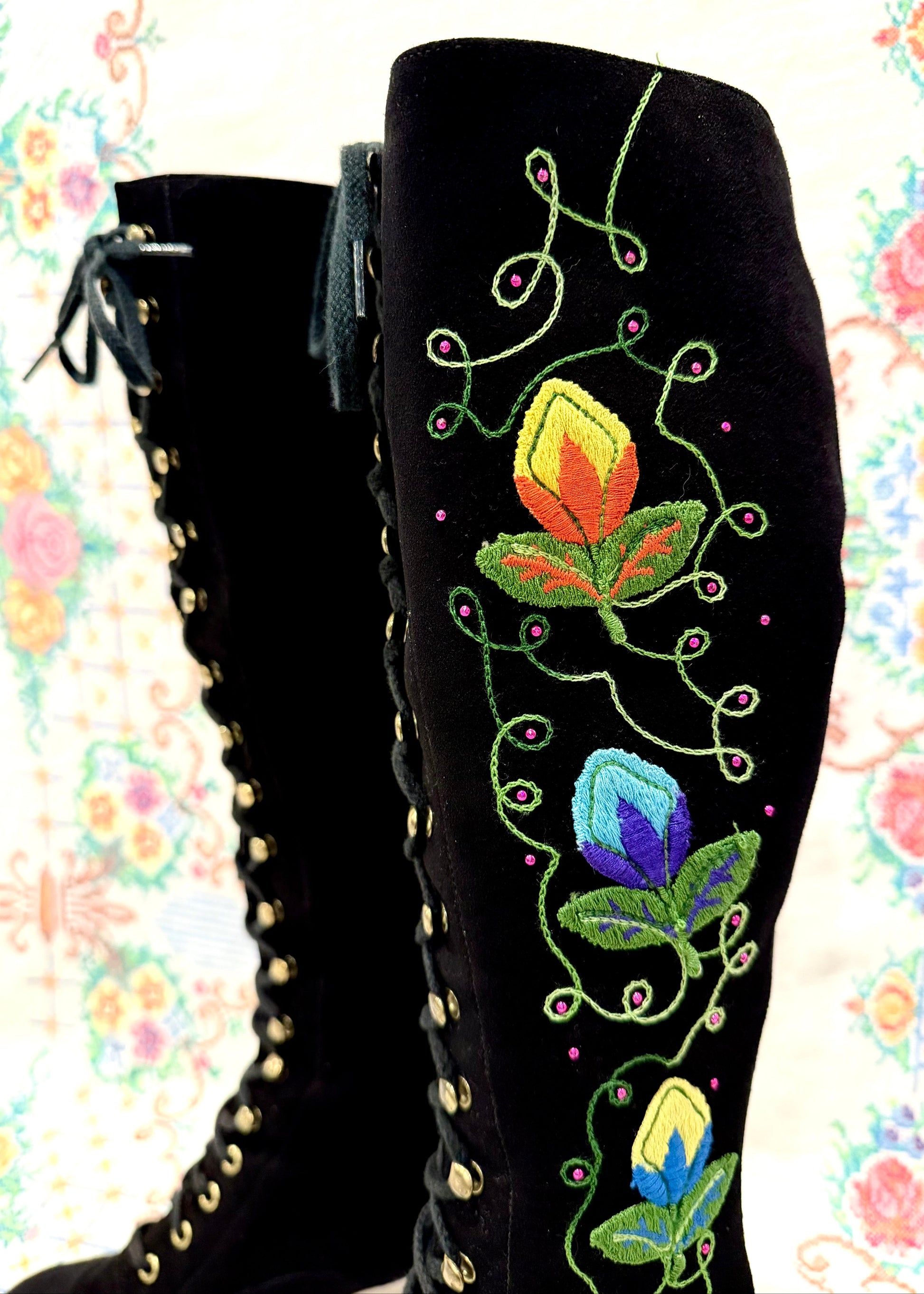 Black knee-high 1960's suede penny lane gogo boots with colorful floral embroidery on a decorative background