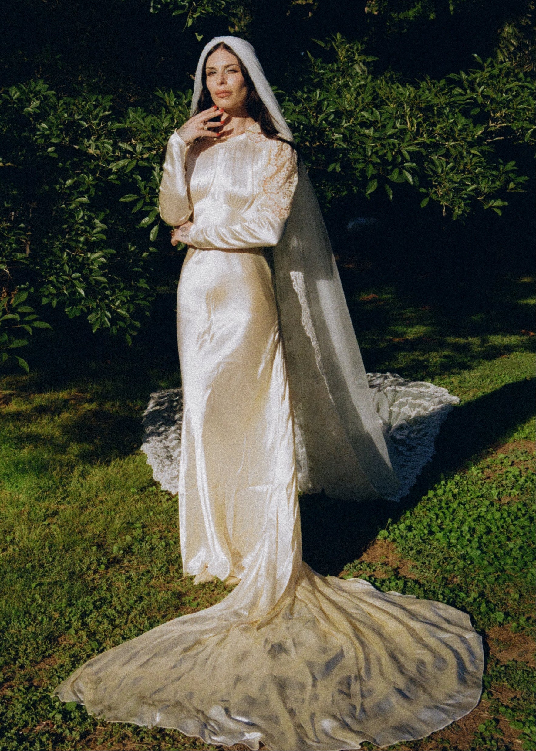Woman in a long, elegant white gown with a cape standing outdoors.