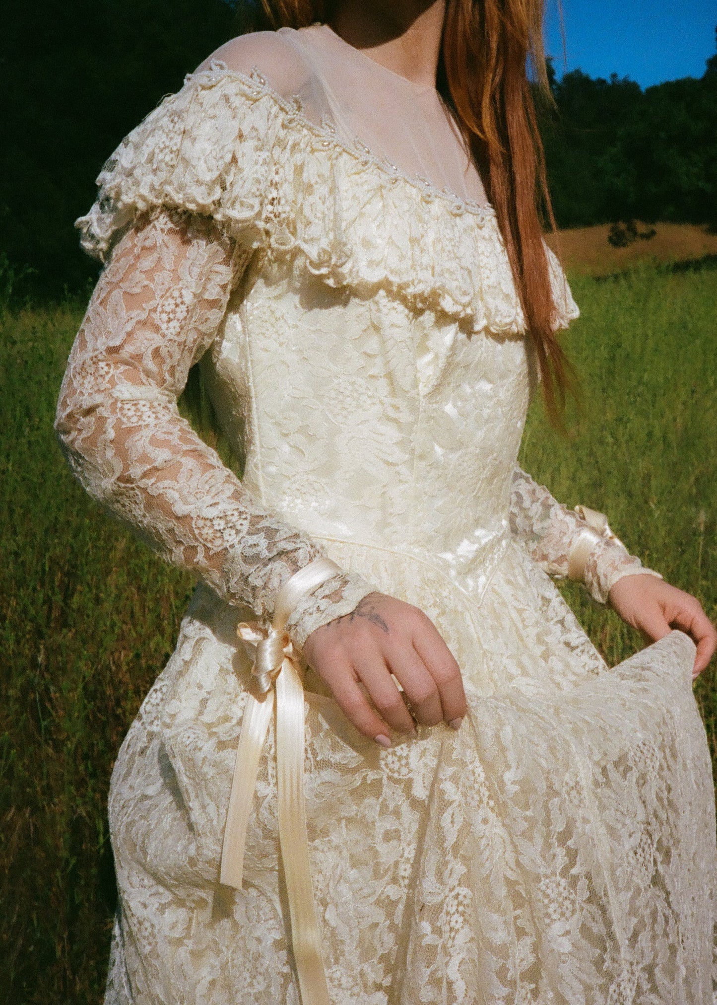 Person wearing a lace dress in a natural setting with greenery.