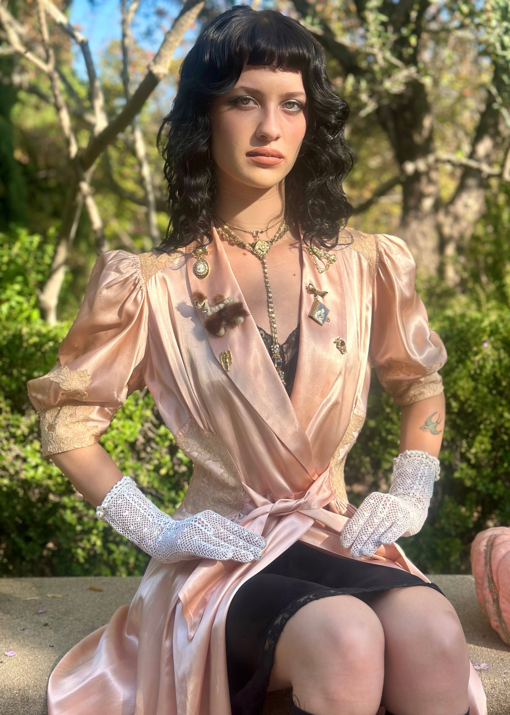 Woman in a vintage-style dress with jewelry and gloves sitting outdoors.