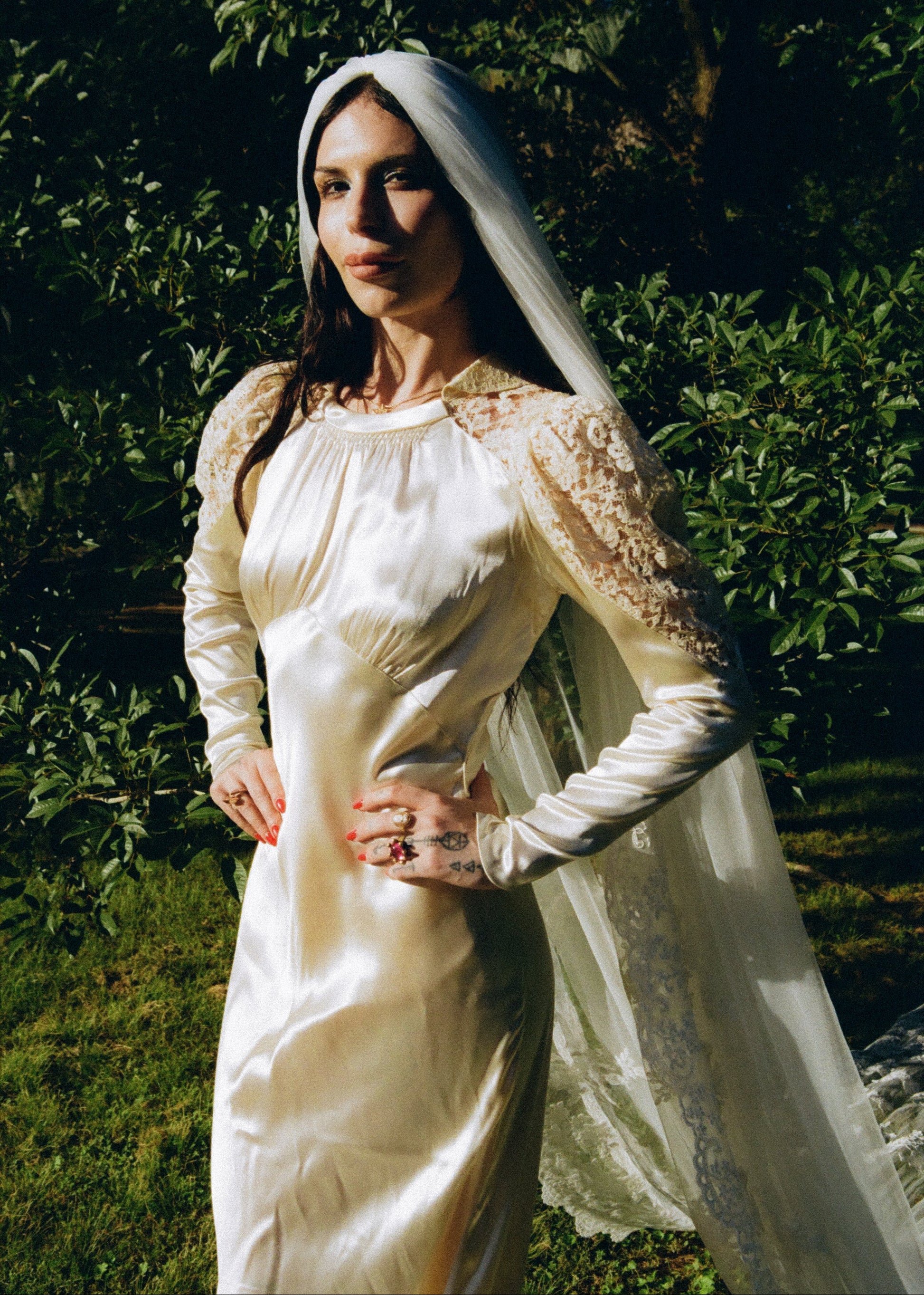 Woman in a white dress with lace sleeves standing outdoors against a green background