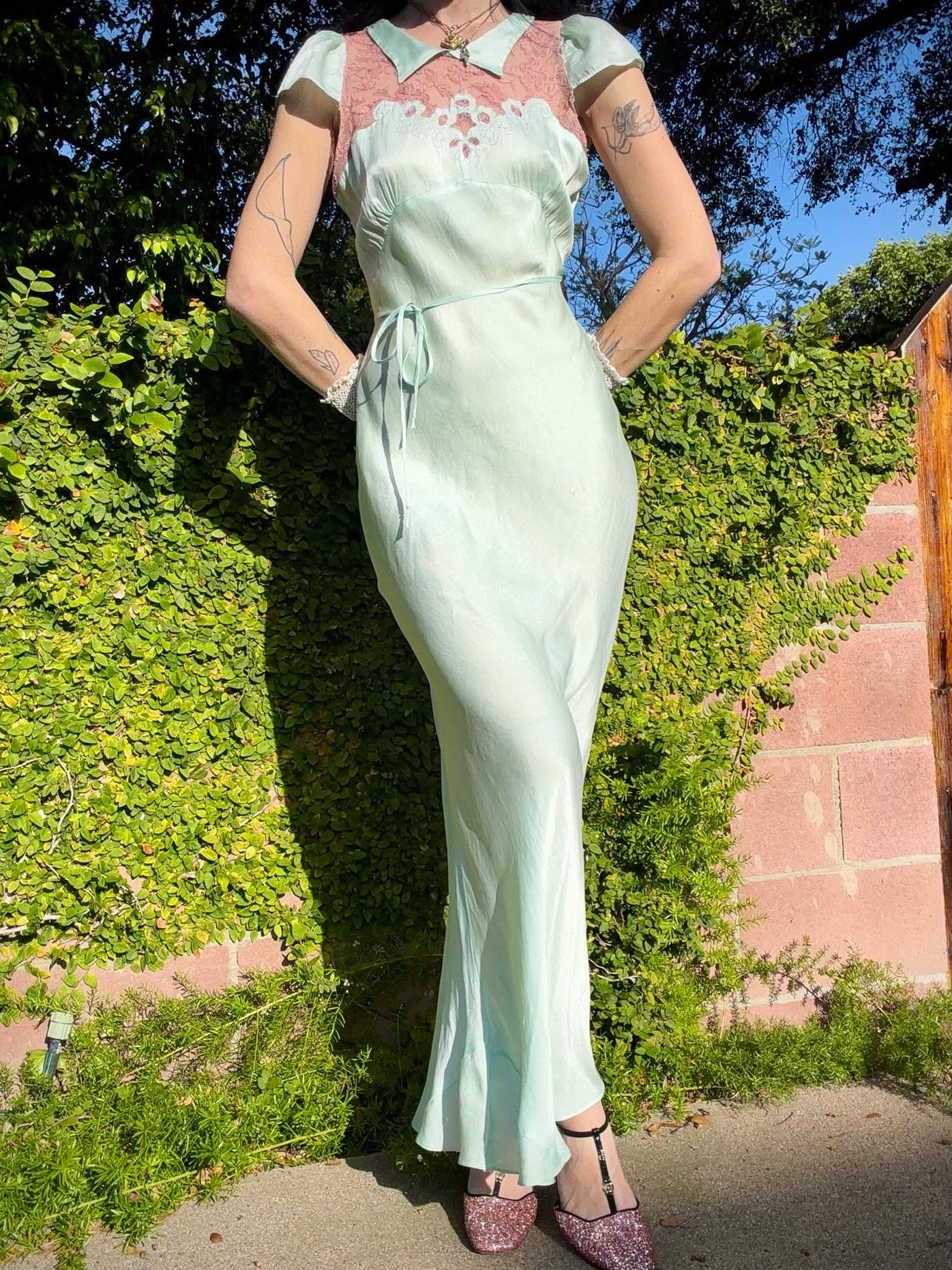 Woman in an antique 1930's silk slip in mint green with a floral headpiece against a wall with framed paintings.