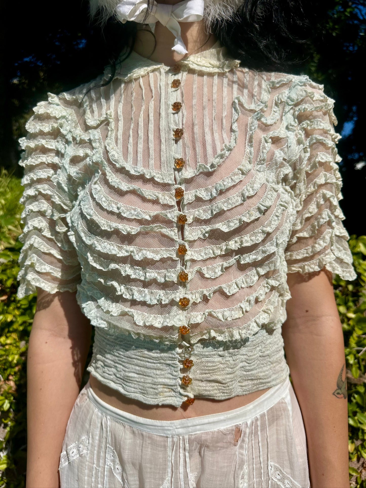 Person wearing a light-colored lace top with buttons outdoors