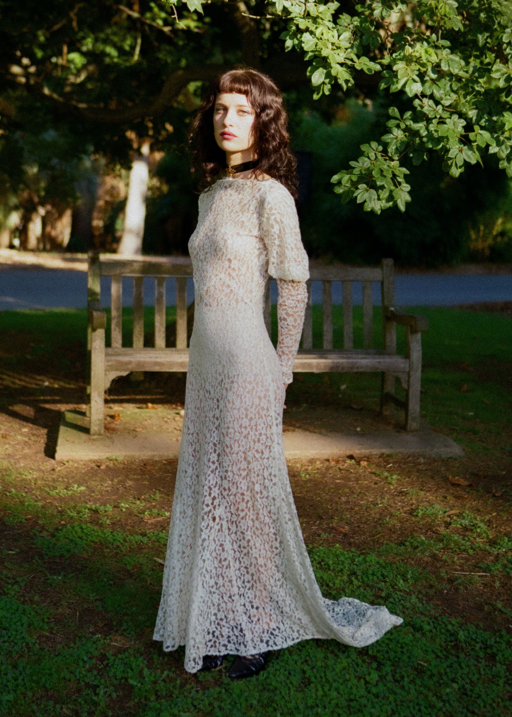 Woman wearing antique lace wedding dress standing outdoors with greenery in the background