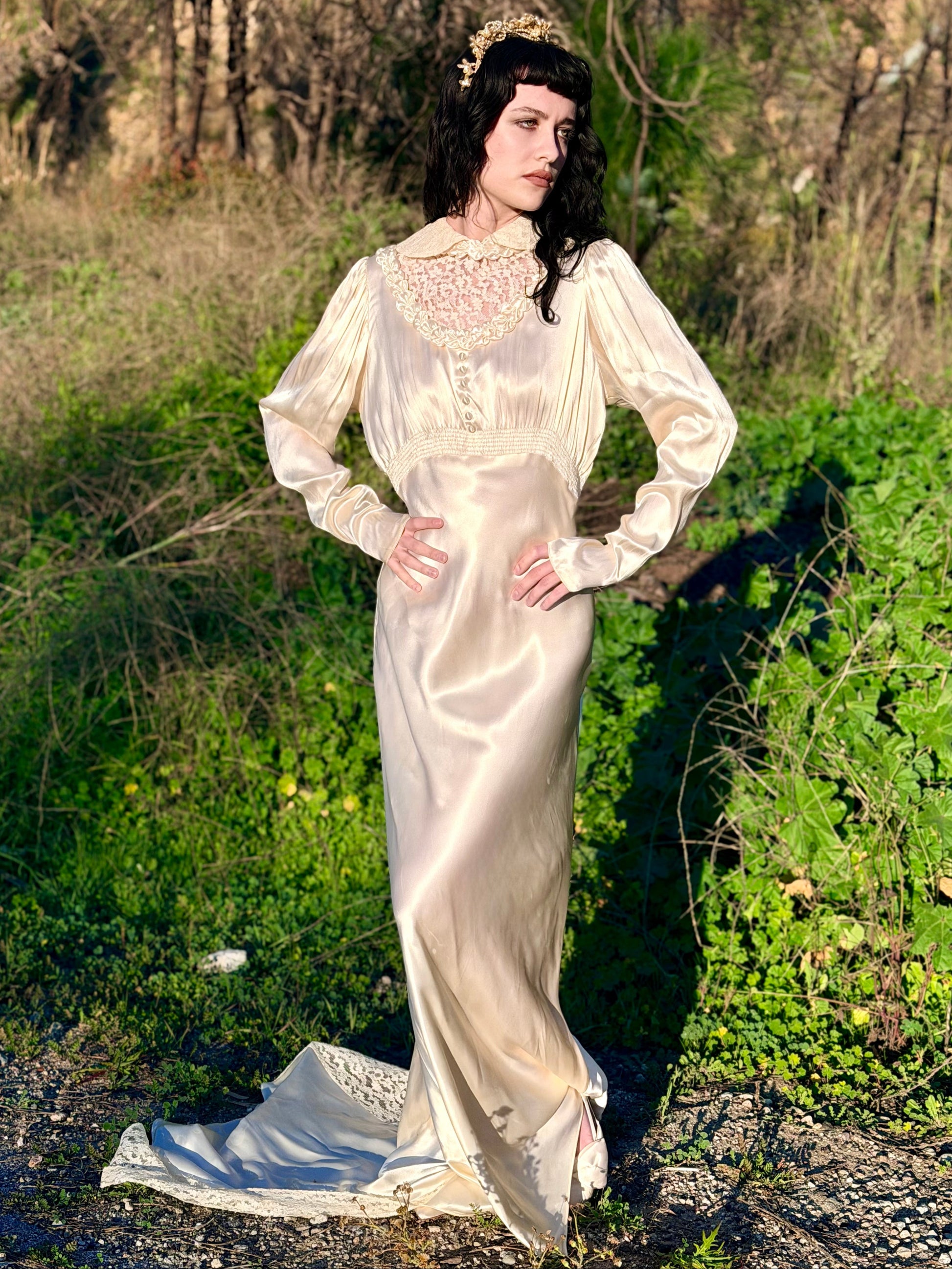 Woman in a long, white vintage dress standing in a natural setting with greenery.