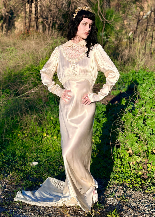Woman in a long, white vintage dress standing in a natural setting with greenery.