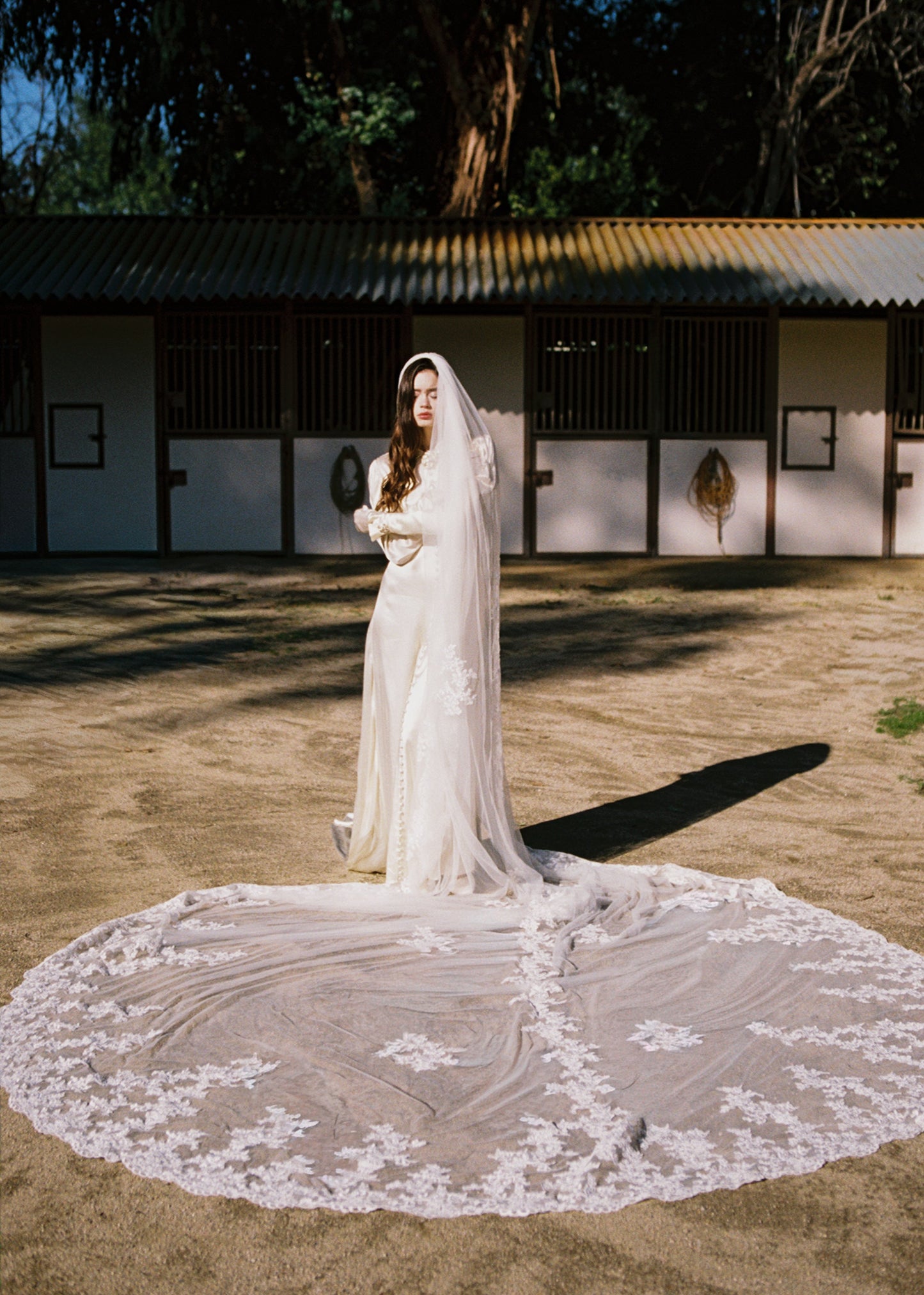Woman in a white wedding dress with a long train standing outdoors.