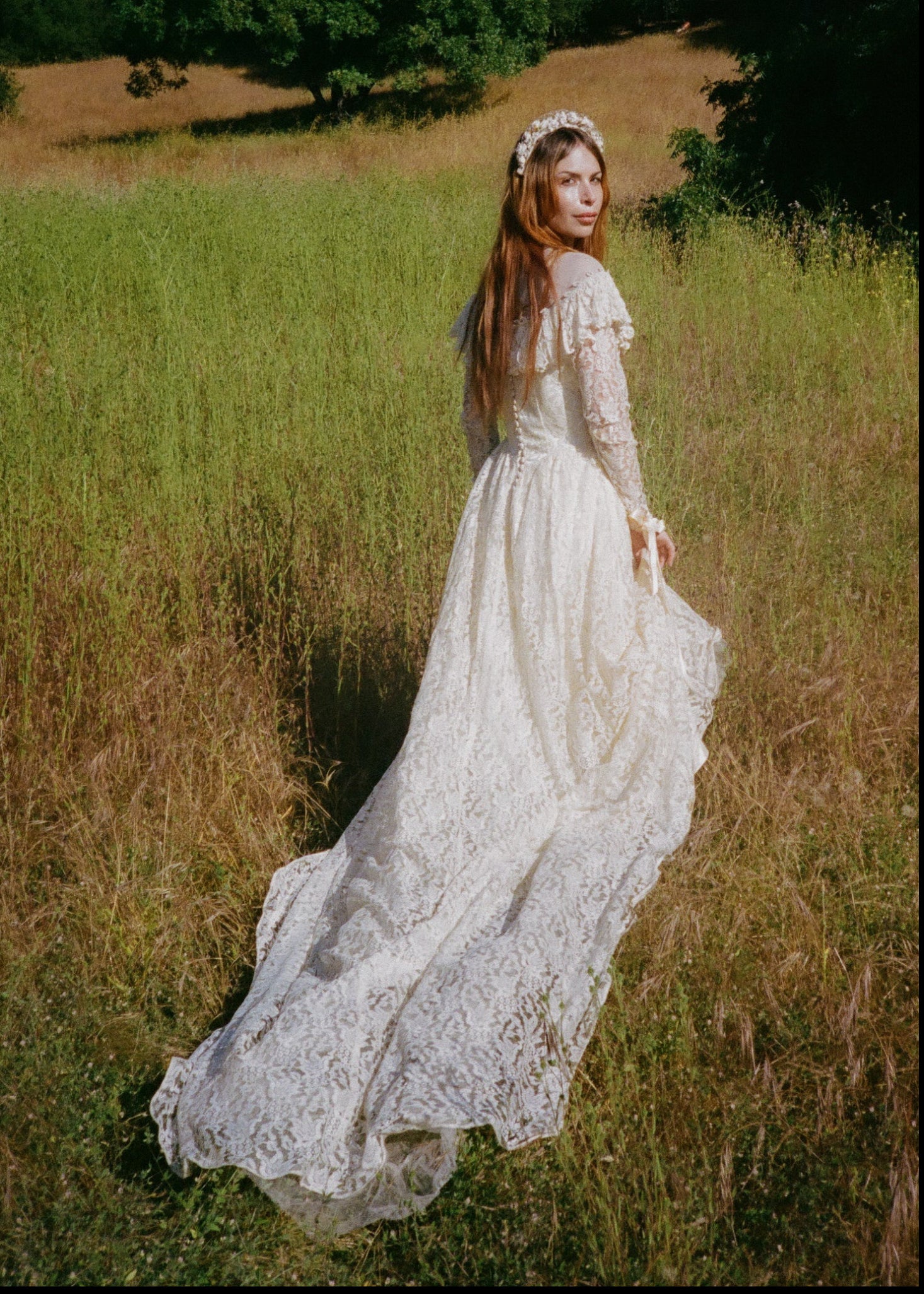 Woman in a white lace dress standing in a field with trees in the background