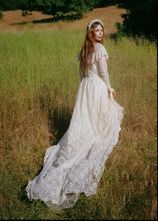 Woman in a white lace dress standing in a field with trees in the background
