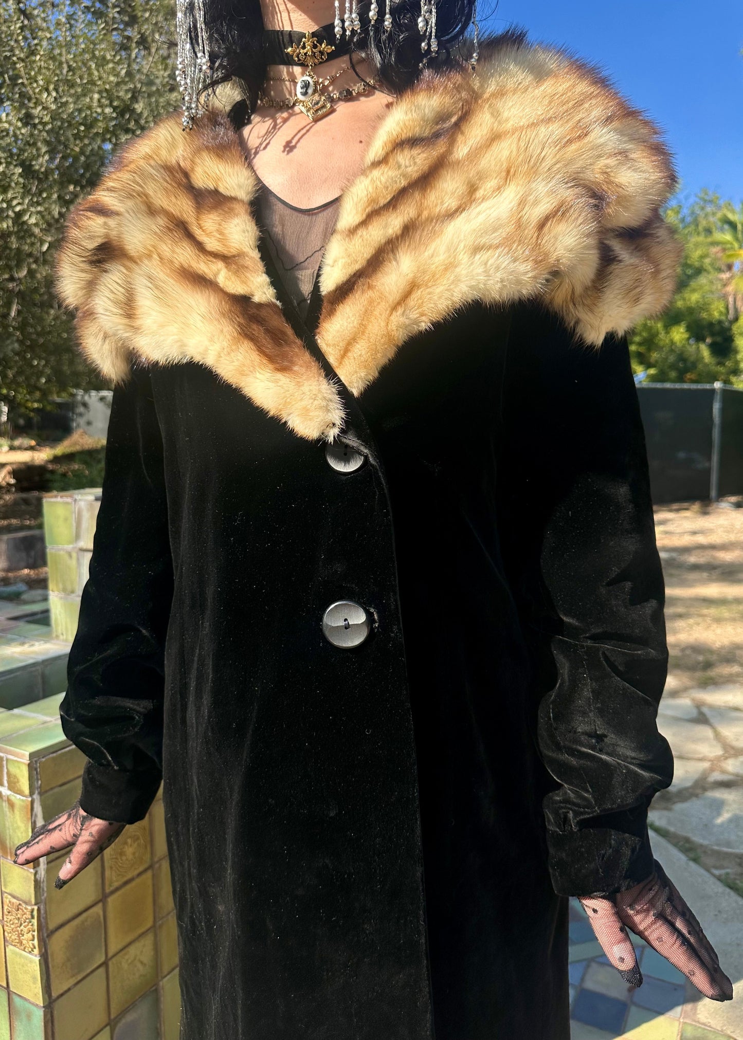 Person wearing a black coat with a fur collar outdoors.