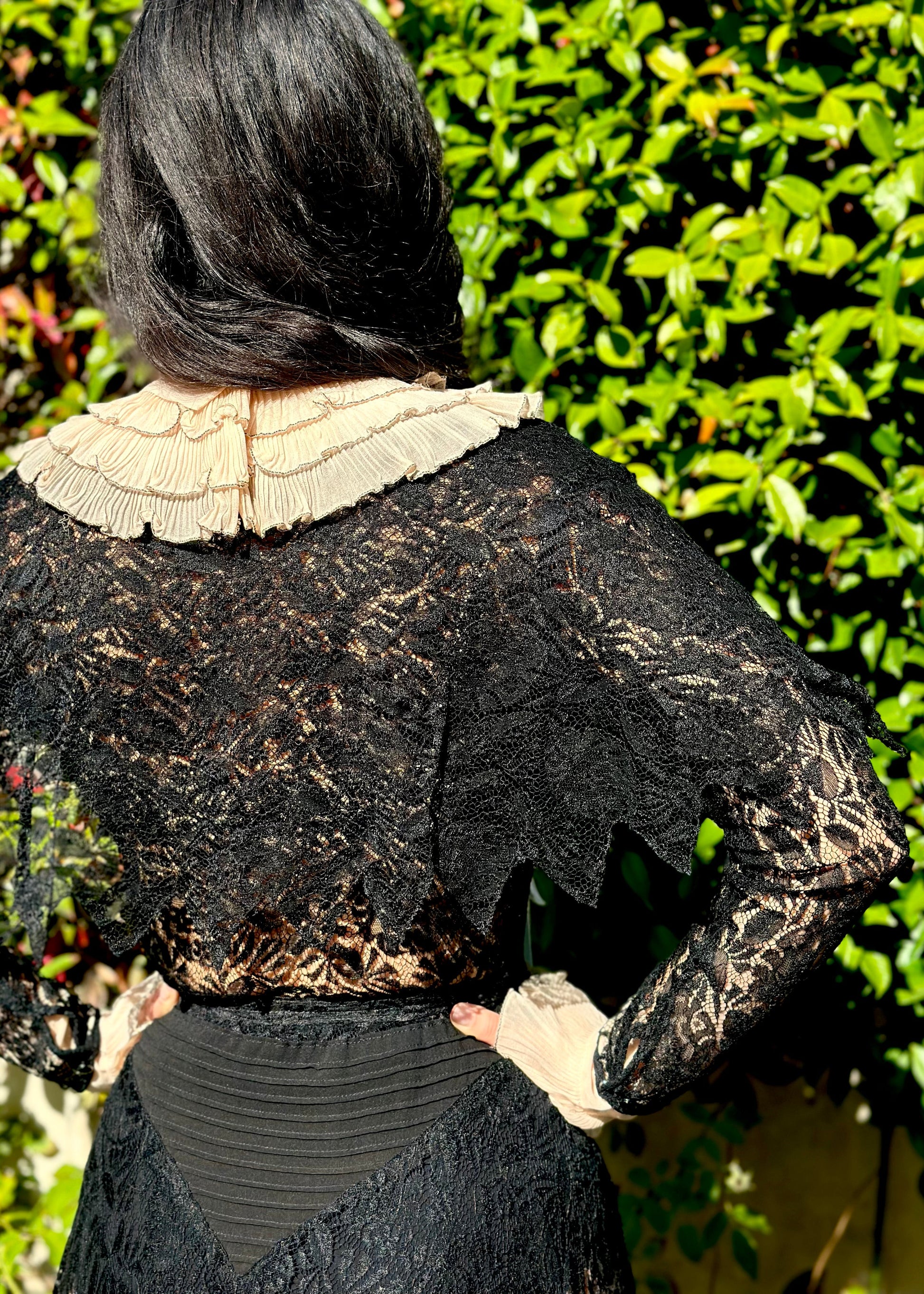 Person wearing a detailed black antique 1920's art deco dress with lace and embroidery, standing in front of an ornate metal gate.