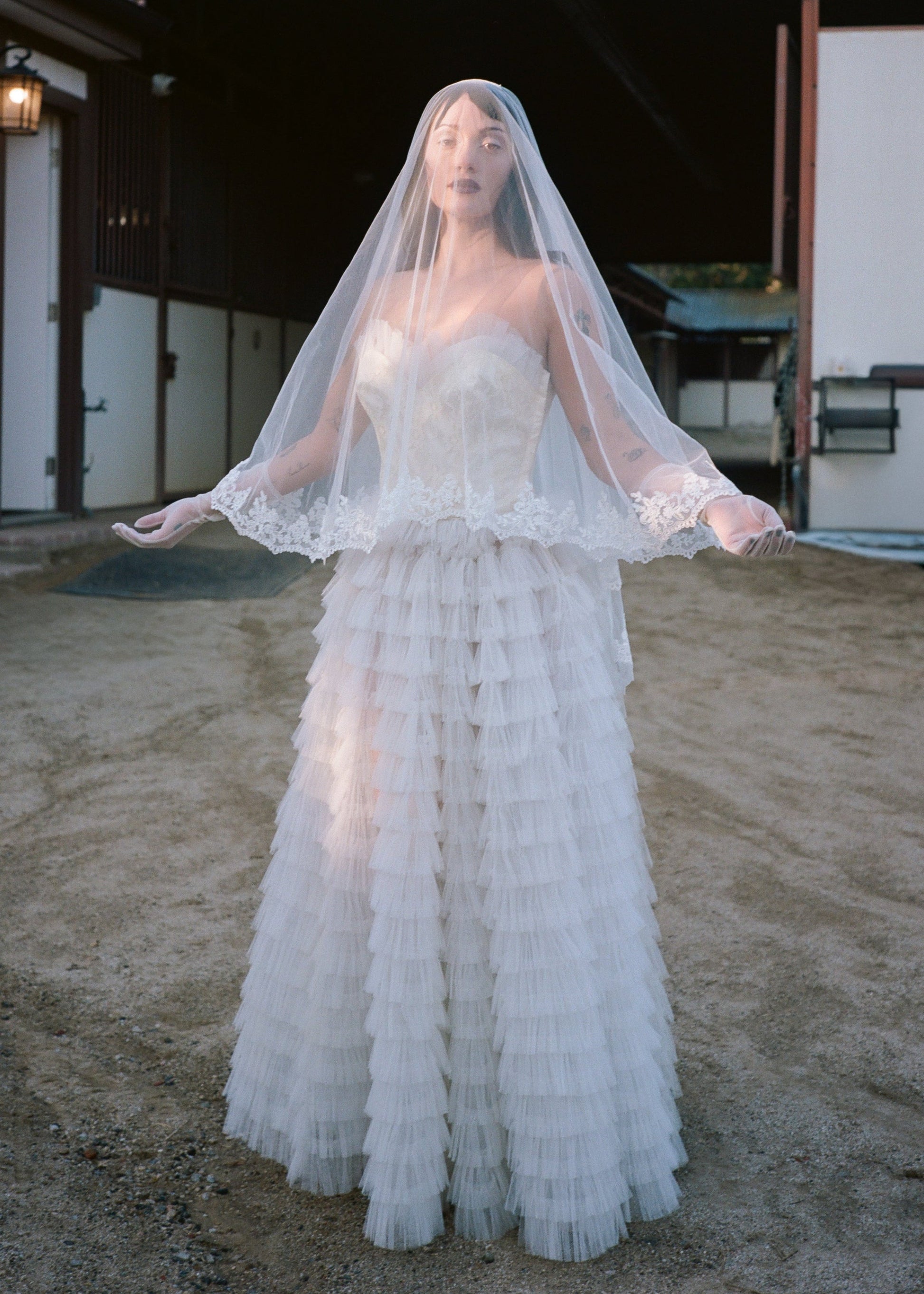 Woman in a vintage wedding dress with a veil standing in front of a rustic building.