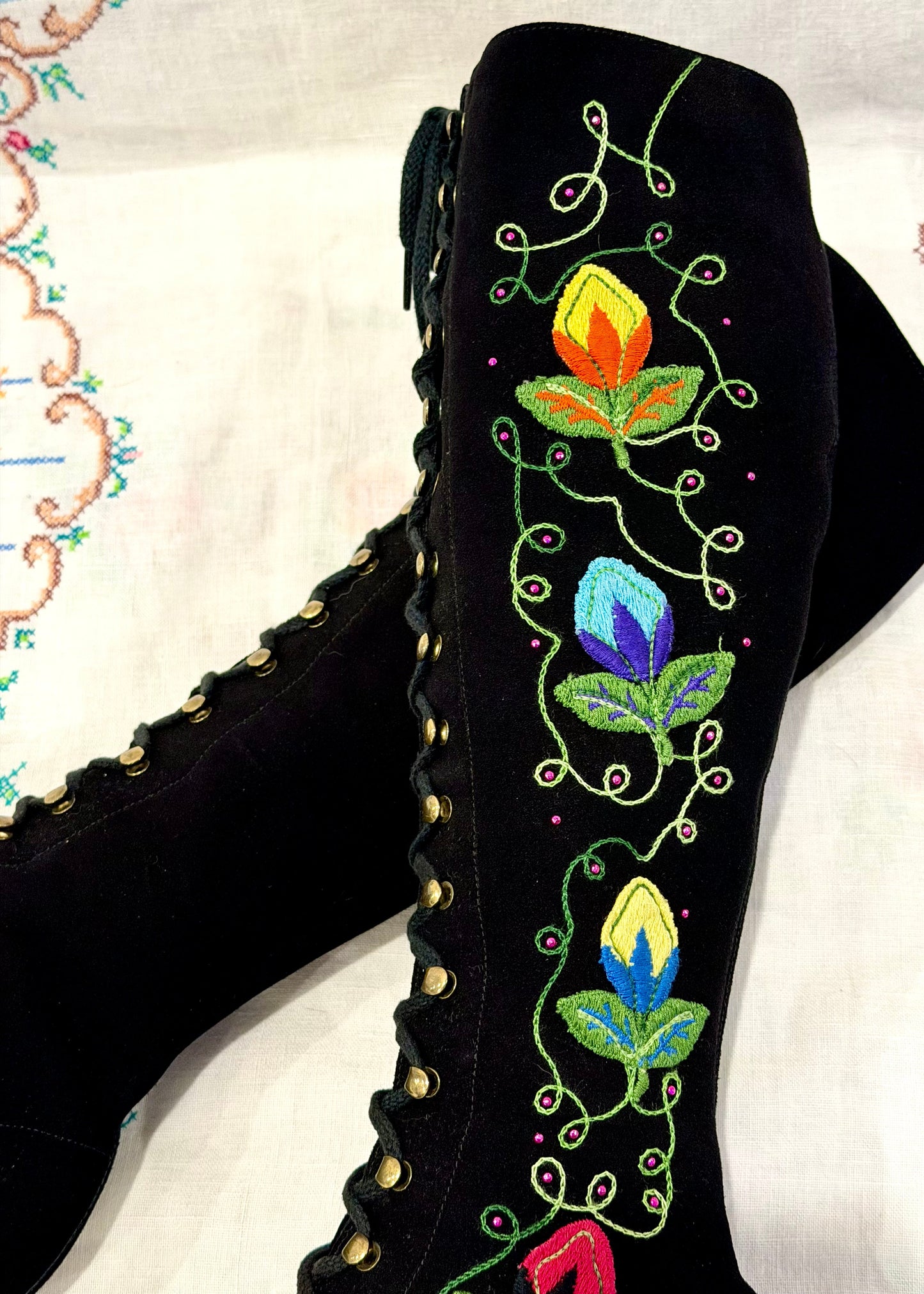 Black knee-high vintage 1960's suede penny lane gogo boots with colorful floral embroidery on a decorative background