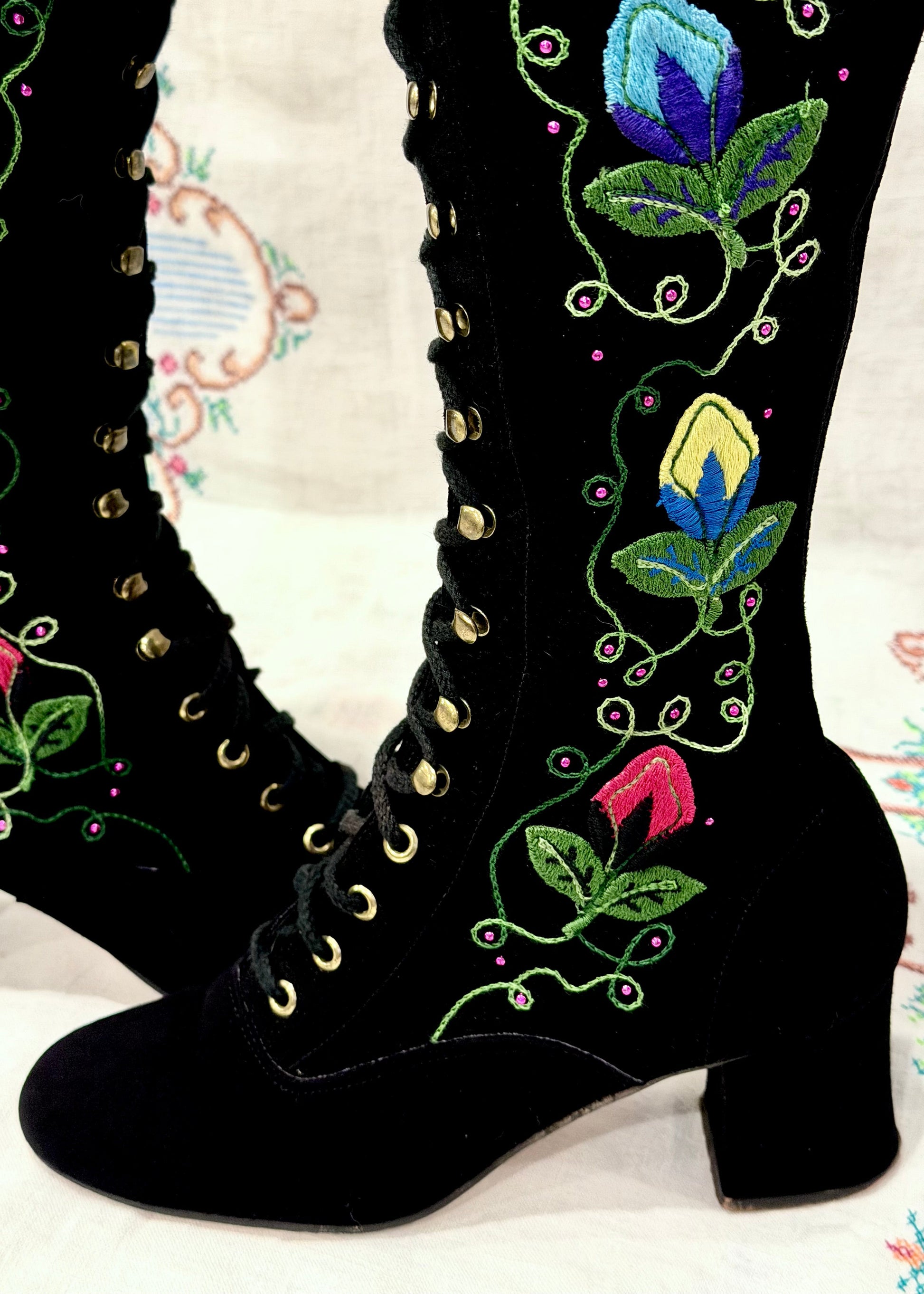 Black knee-high vintage 1960's suede penny lane gogo boots with colorful floral embroidery on a decorative background