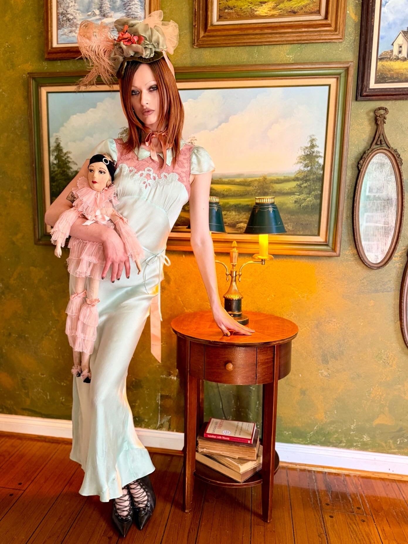 Woman in an antique 1930's silk slip in mint green with a floral headpiece against a wall with framed paintings.
