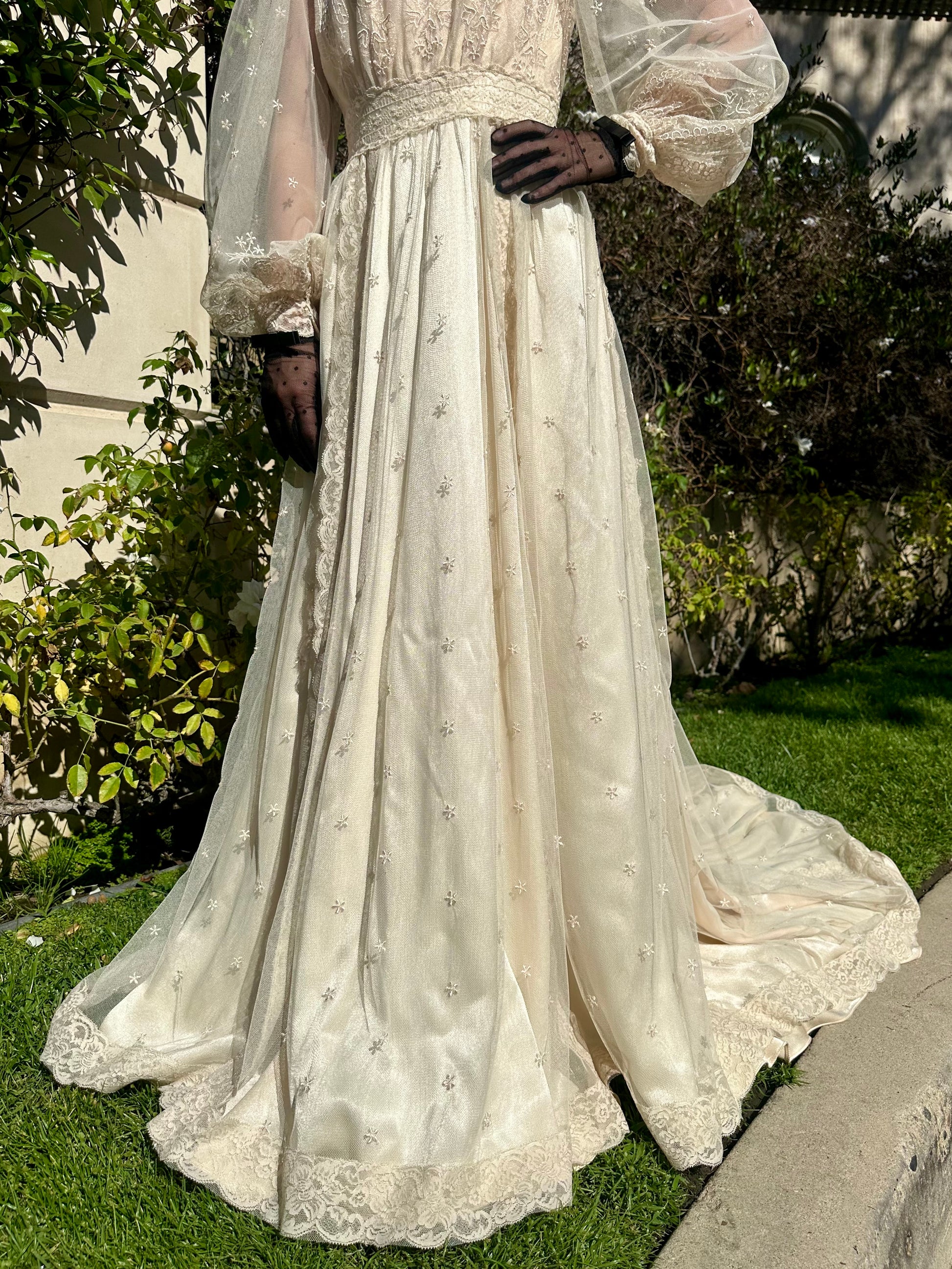 Elegant white lace dress with long sleeves and a flowing skirt on a grassy outdoor setting.