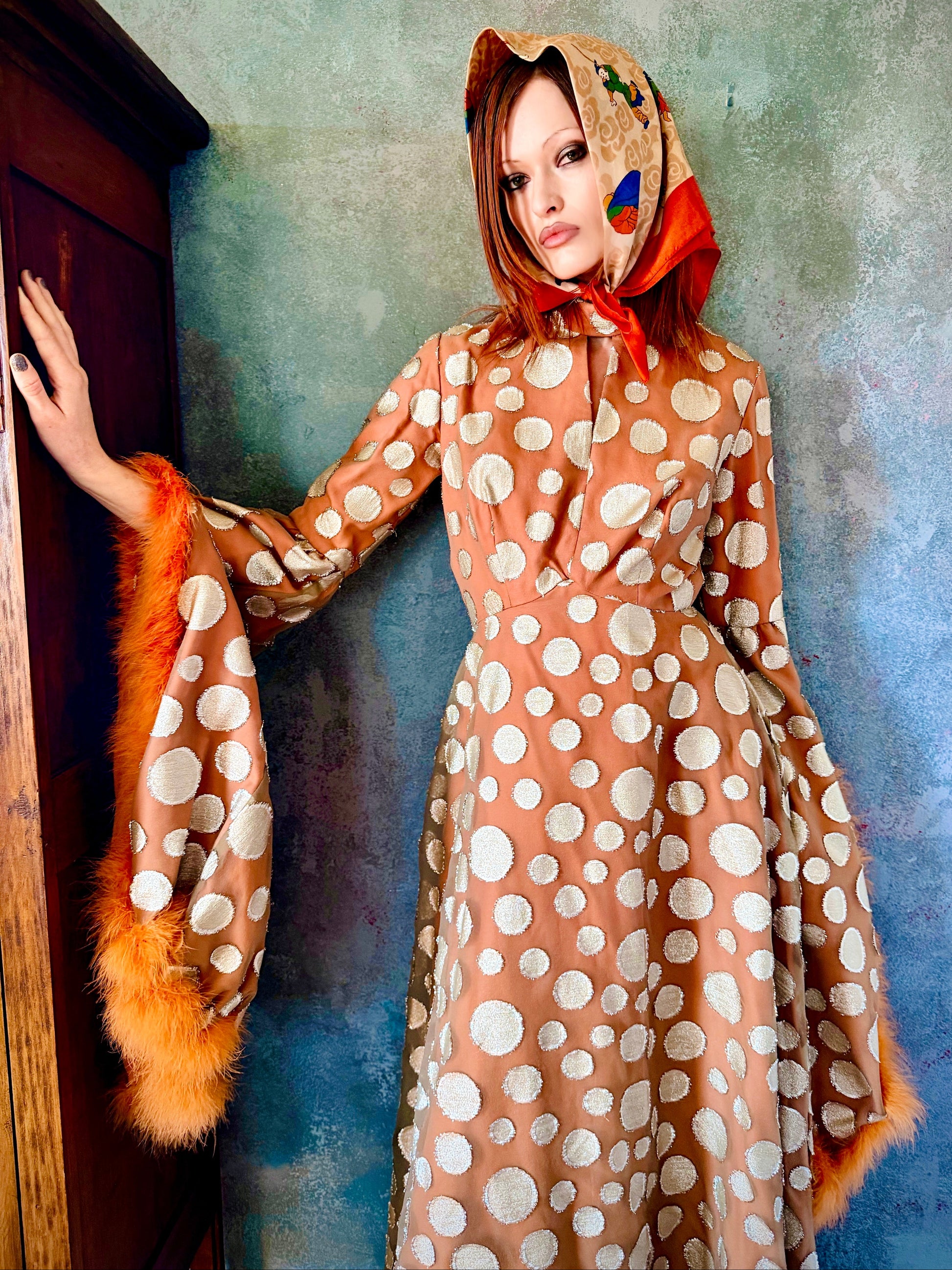 Woman in a vintage 1970's chiffon polka dot maxi dress with marabou feather accents standing outdoors.