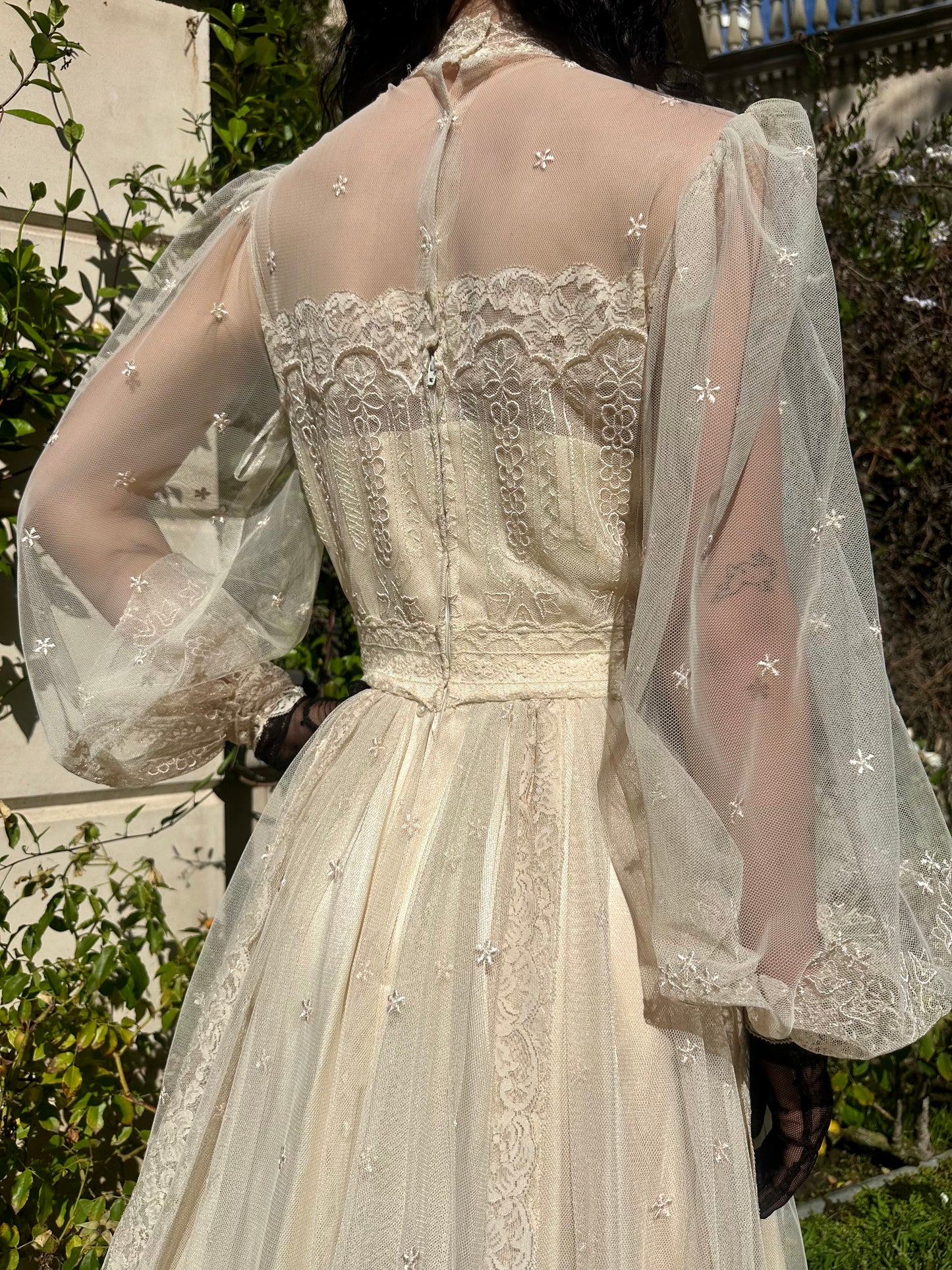 Elegant white lace dress with sheer sleeves against a blurred natural background