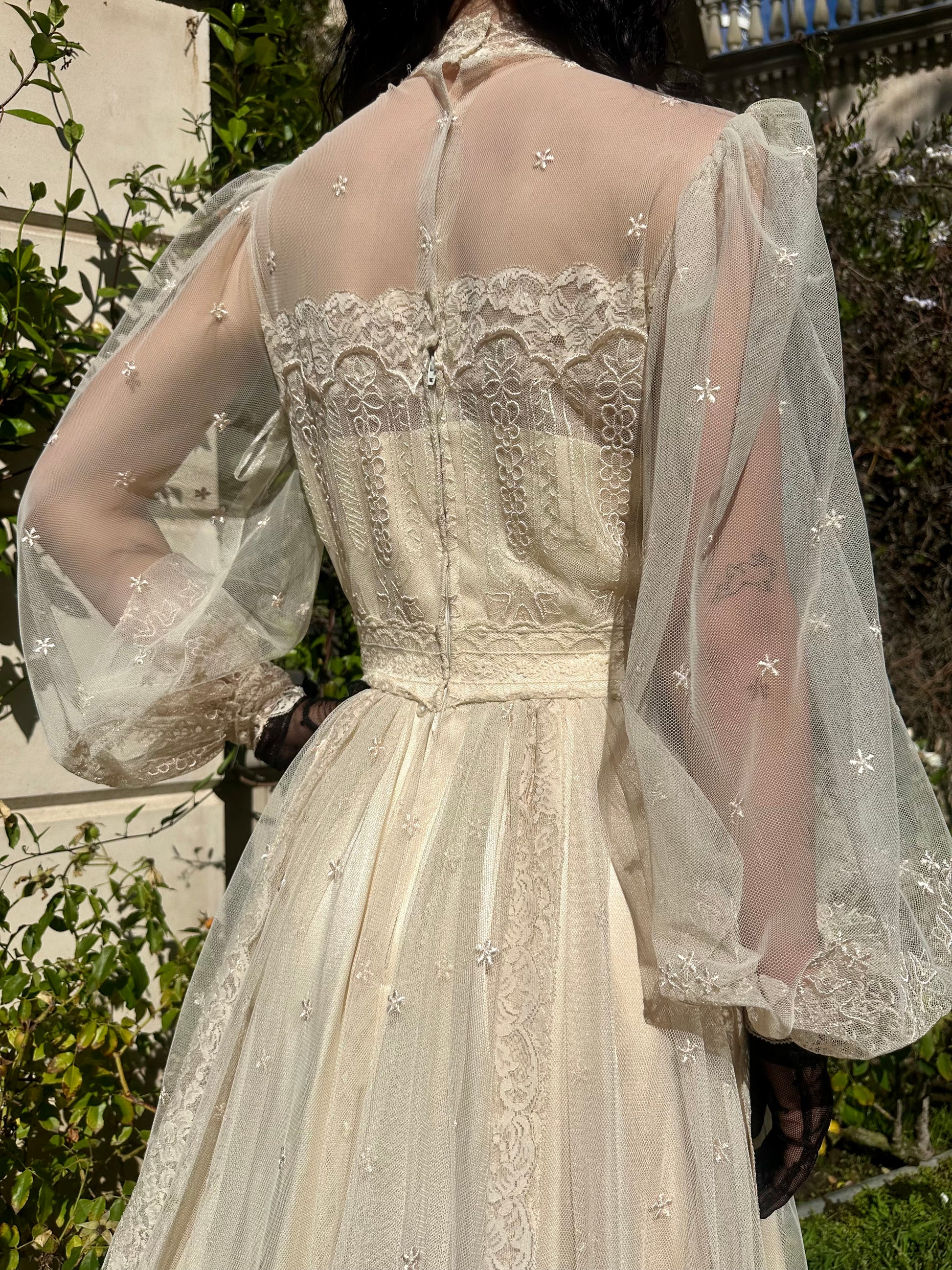 Elegant white lace dress with sheer sleeves against a blurred natural background