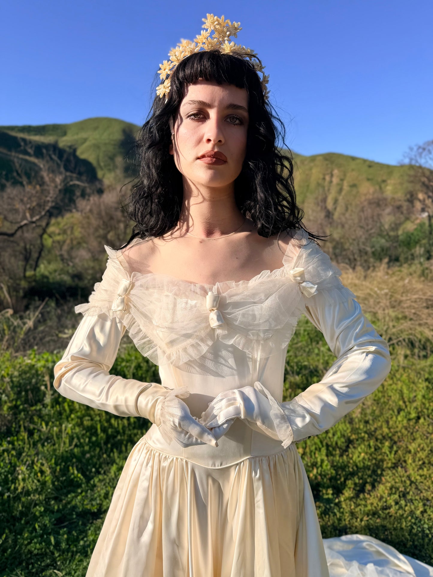 Woman in a historical dress with a floral headpiece standing outdoors with mountains in the background