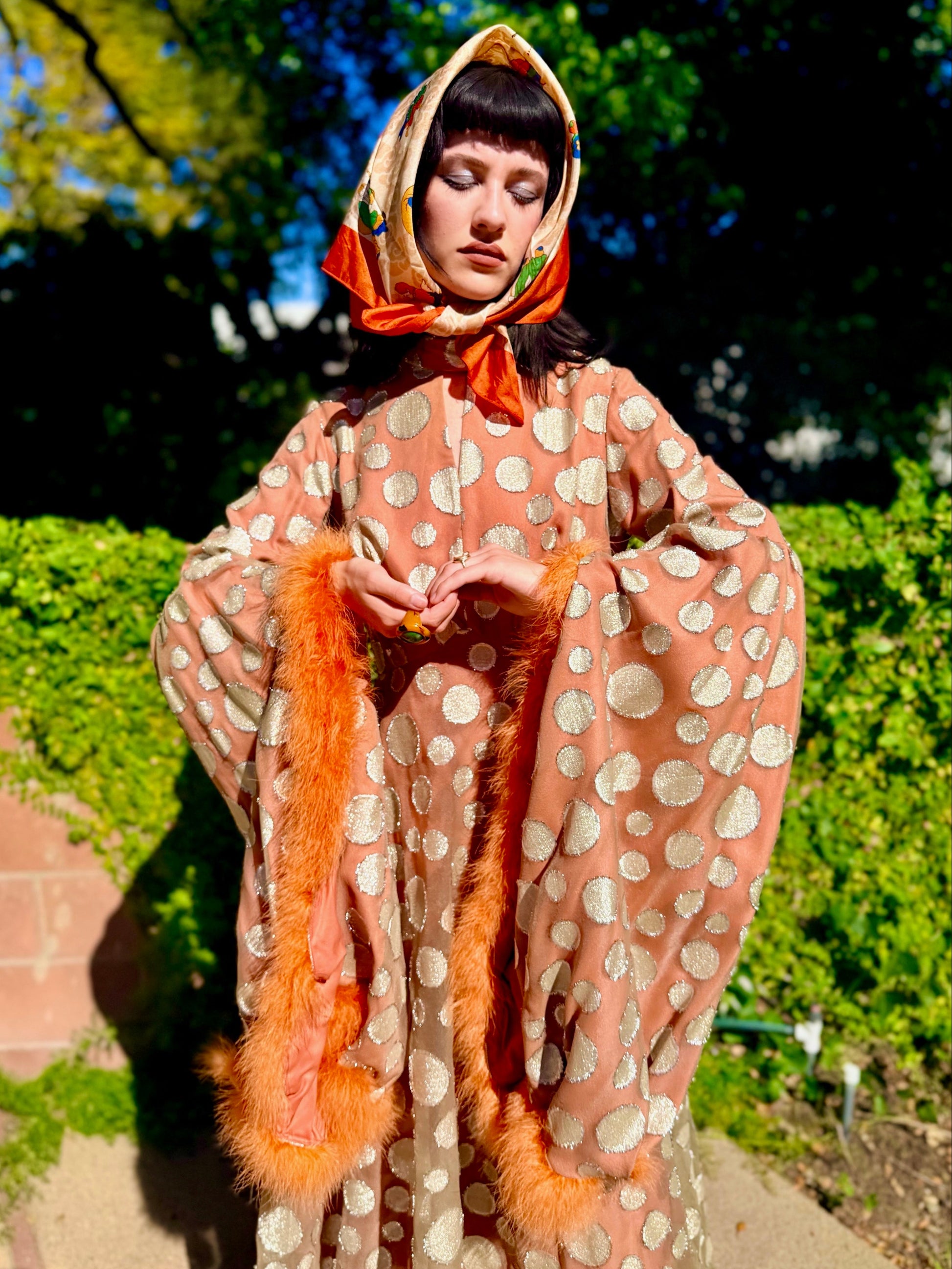 Woman in a vintage 1970s disco glamorous maxi dress with polka dots and orange accents standing outdoors.