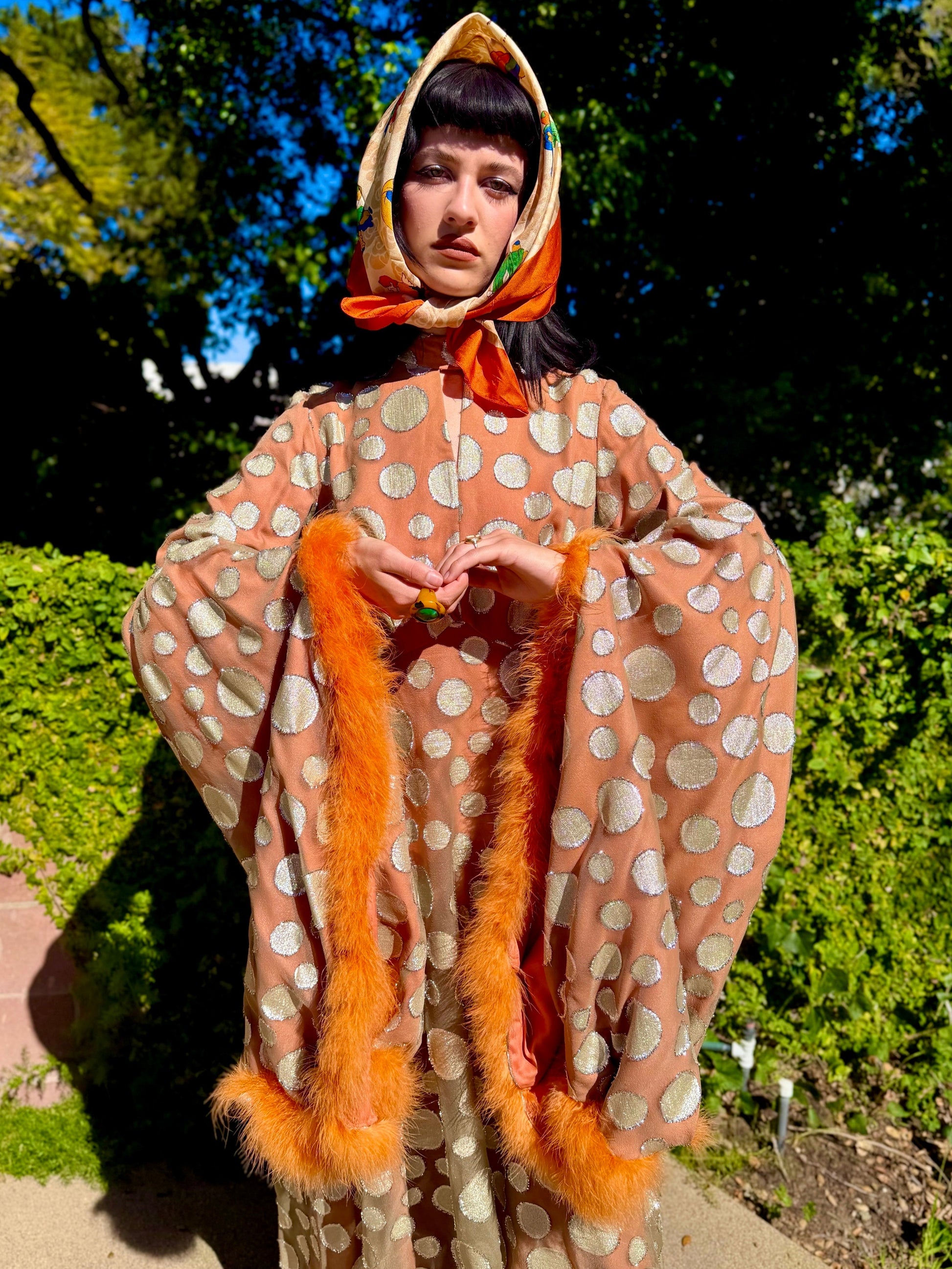 Woman in a vintage 1970s disco glamorous maxi dress with polka dots and orange accents standing outdoors.