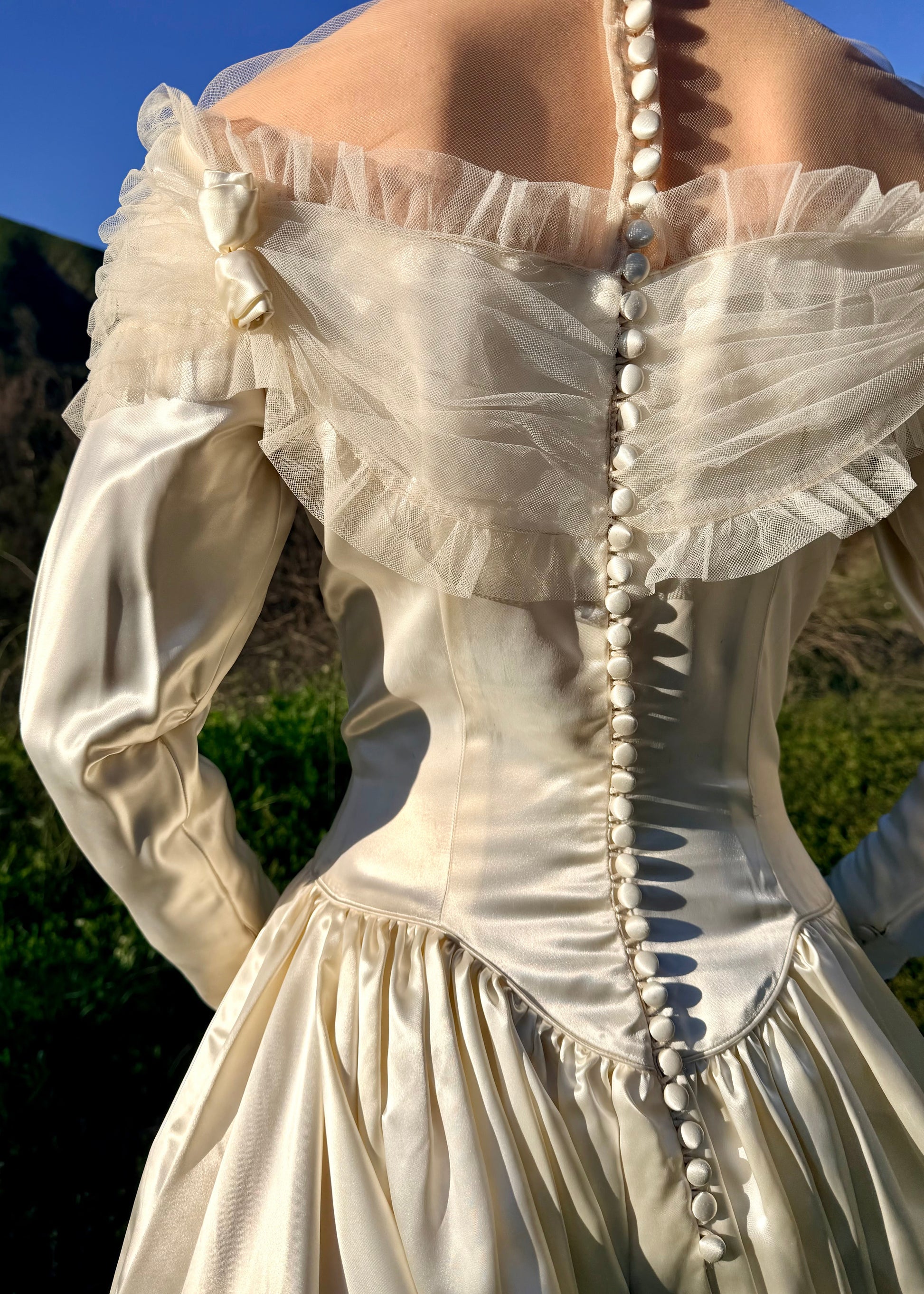 Close-up of a white dress with long sleeves and pearl buttons against a blurred natural background
